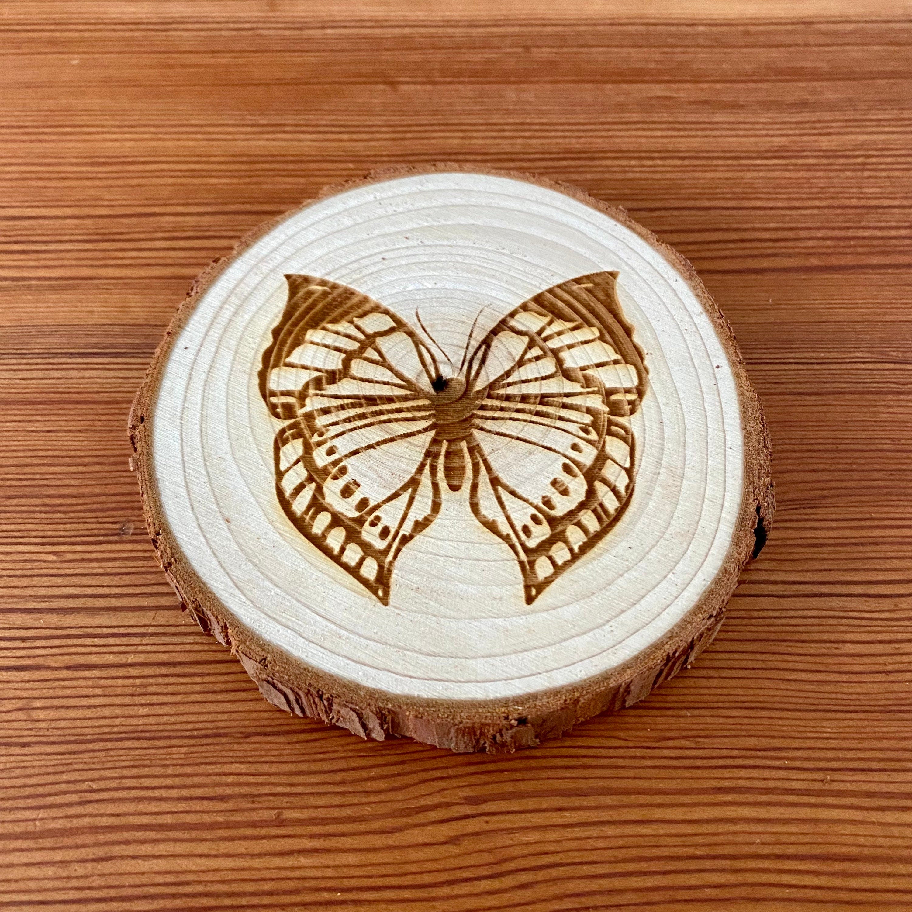 A set of four butterfly engraved wood coasters on a rustic wooden table, showcasing intricate butterfly designs.