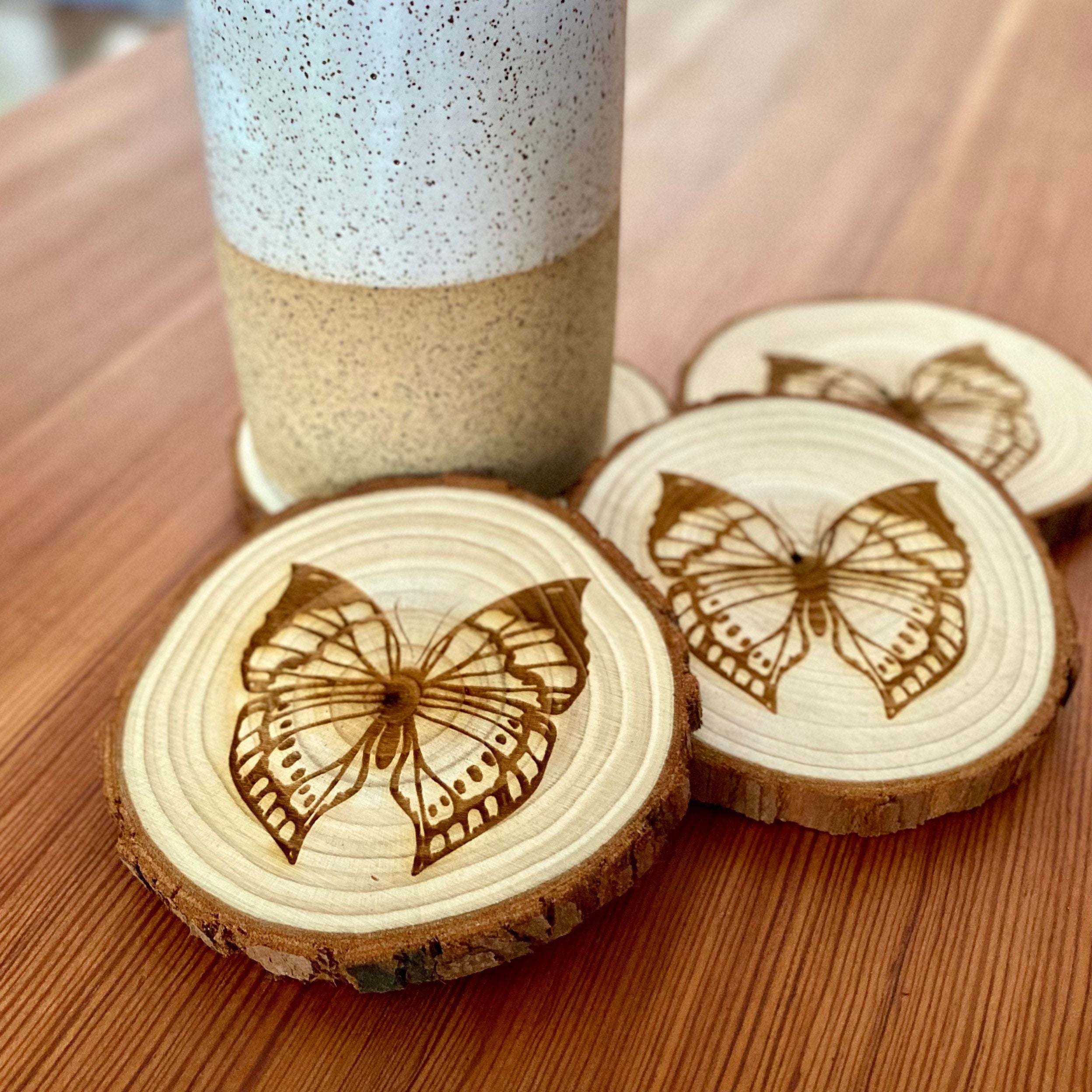 A set of four butterfly engraved wood coasters on a rustic wooden table, showcasing intricate butterfly designs.