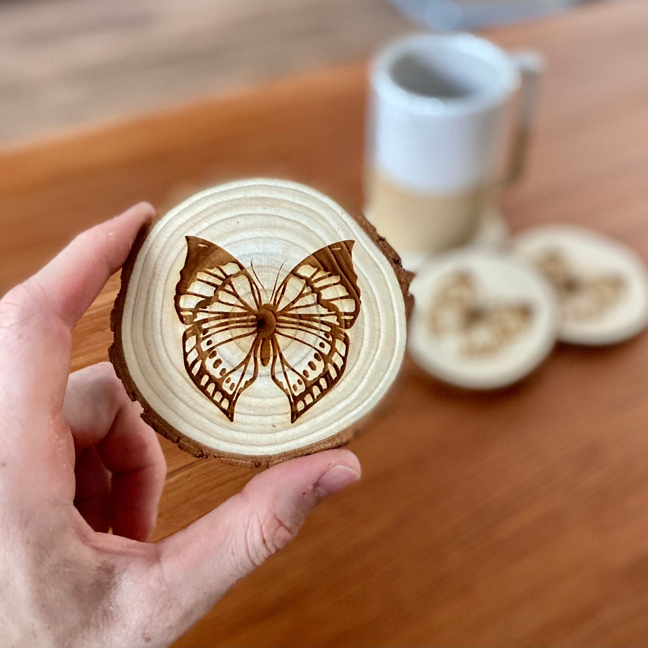 A set of four butterfly engraved wood coasters on a rustic wooden table, showcasing intricate butterfly designs.