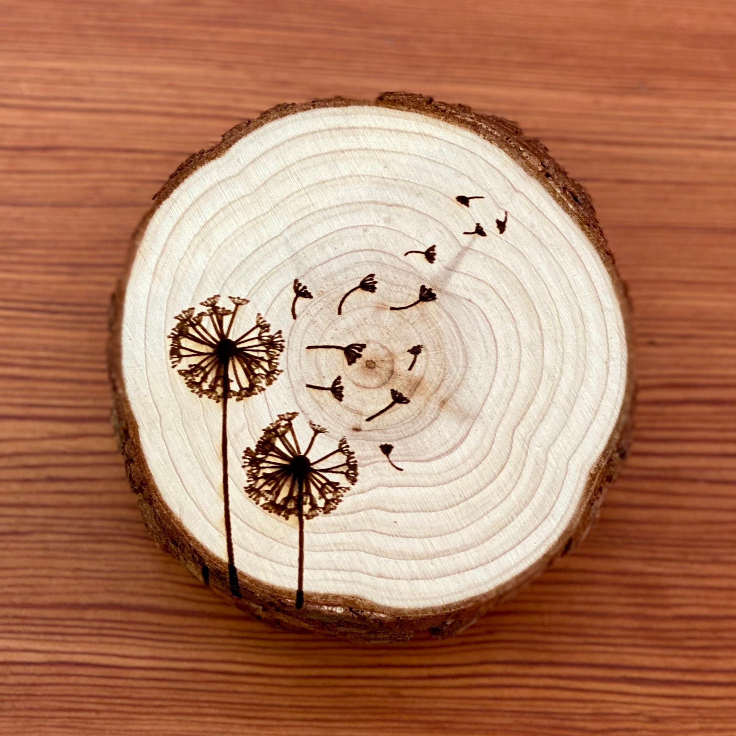 A set of four laser engraved wood coasters featuring intricate dandelion designs, showcasing their natural wood finish and unique textures.