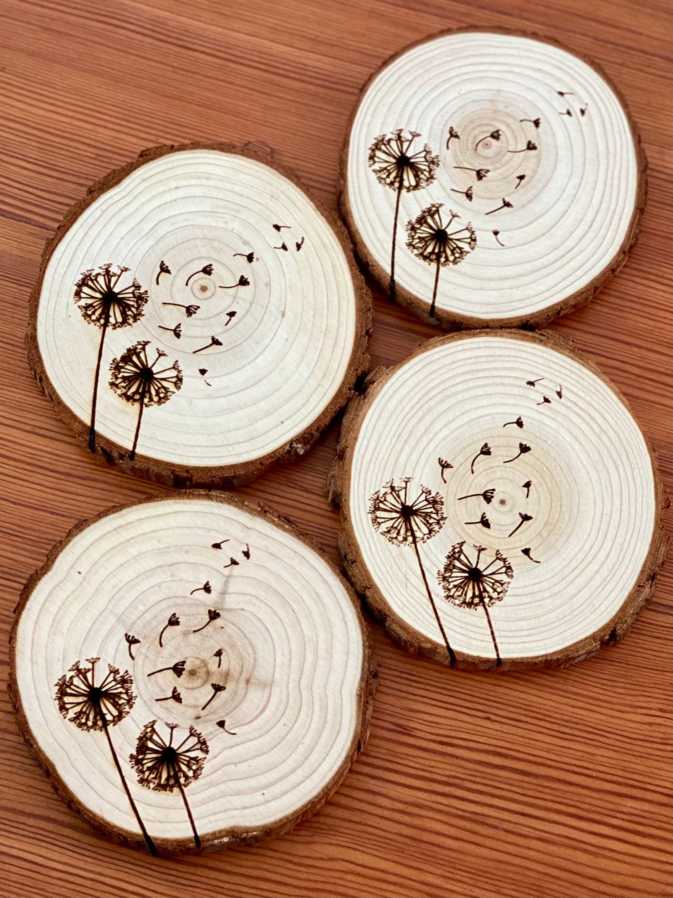 A set of four laser engraved wood coasters featuring intricate dandelion designs, showcasing their natural wood finish and unique textures.