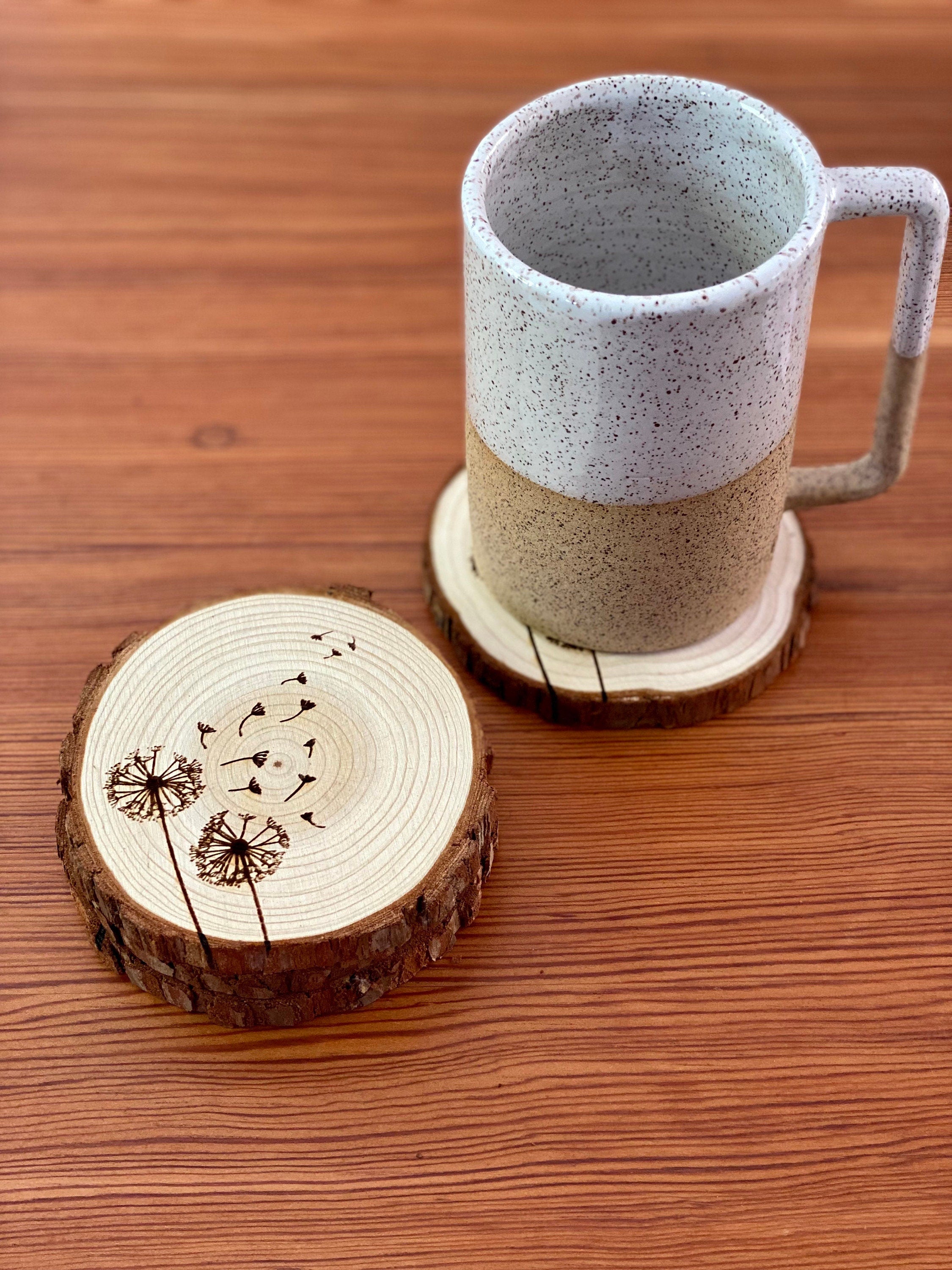 A set of four laser engraved wood coasters featuring intricate dandelion designs, showcasing their natural wood finish and unique textures.