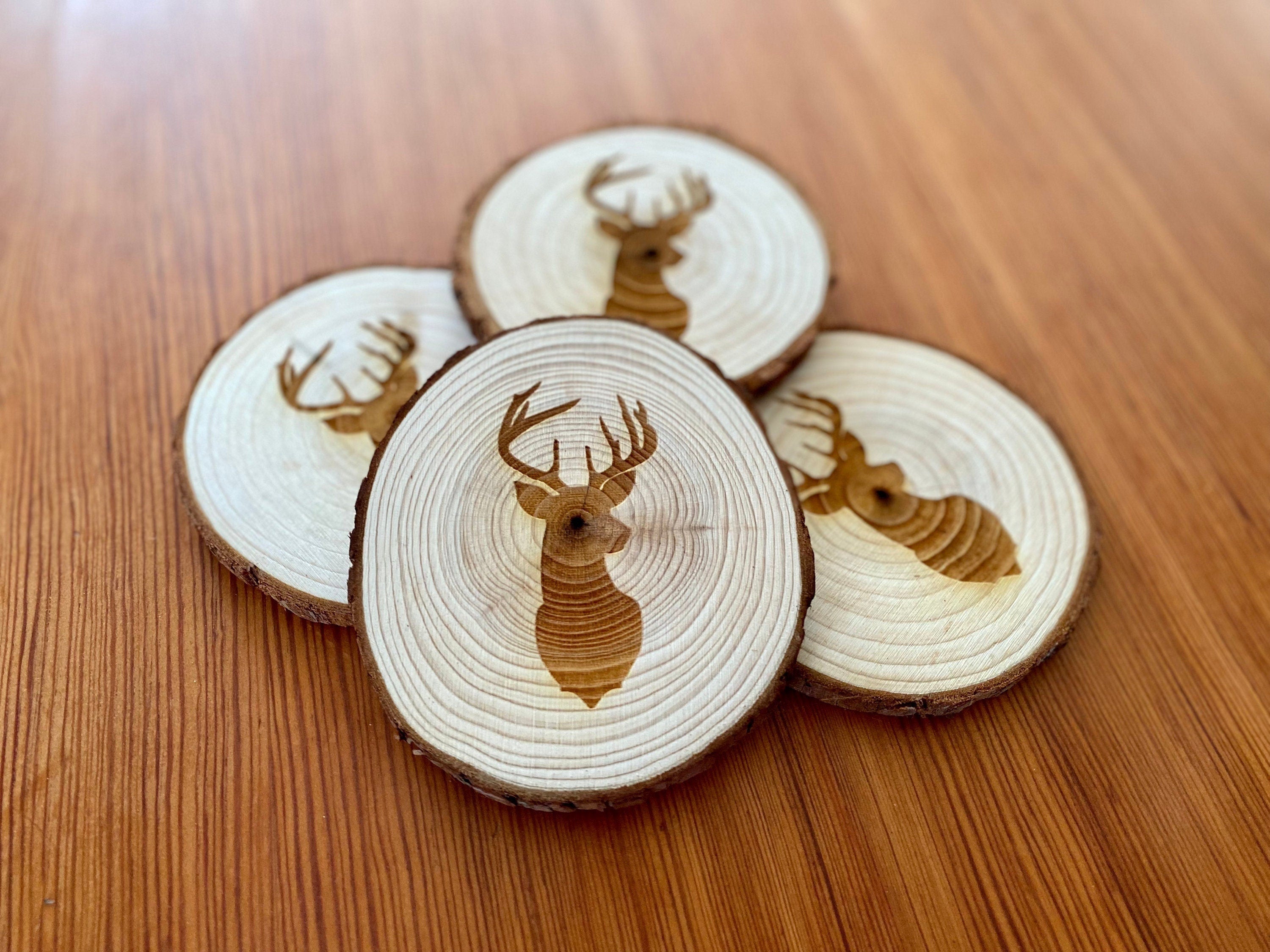 A set of four laser engraved wood coasters featuring a deer head silhouette, showcasing their natural wood finish and unique design.