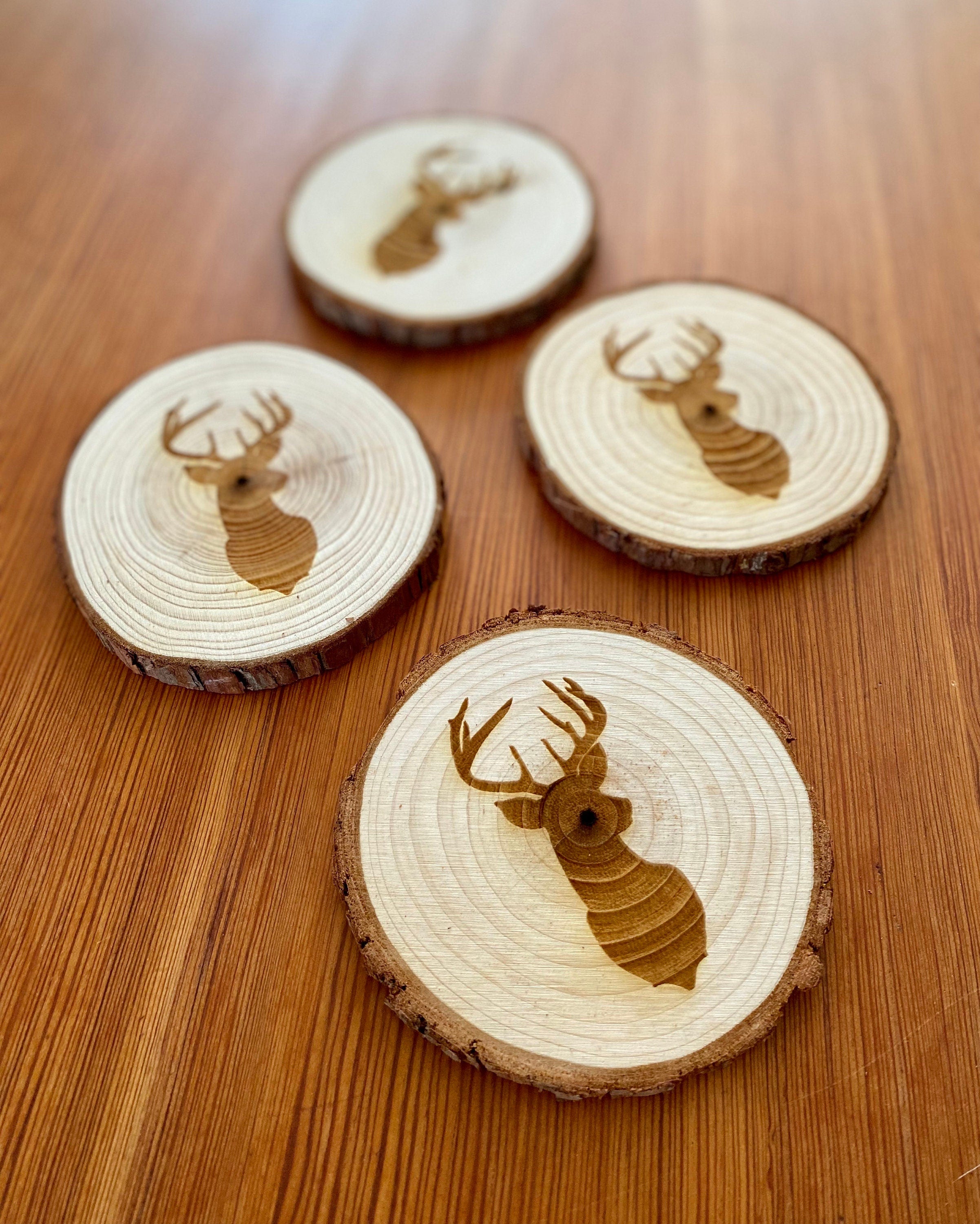 A set of four laser engraved wood coasters featuring a deer head silhouette, showcasing their natural wood finish and unique design.