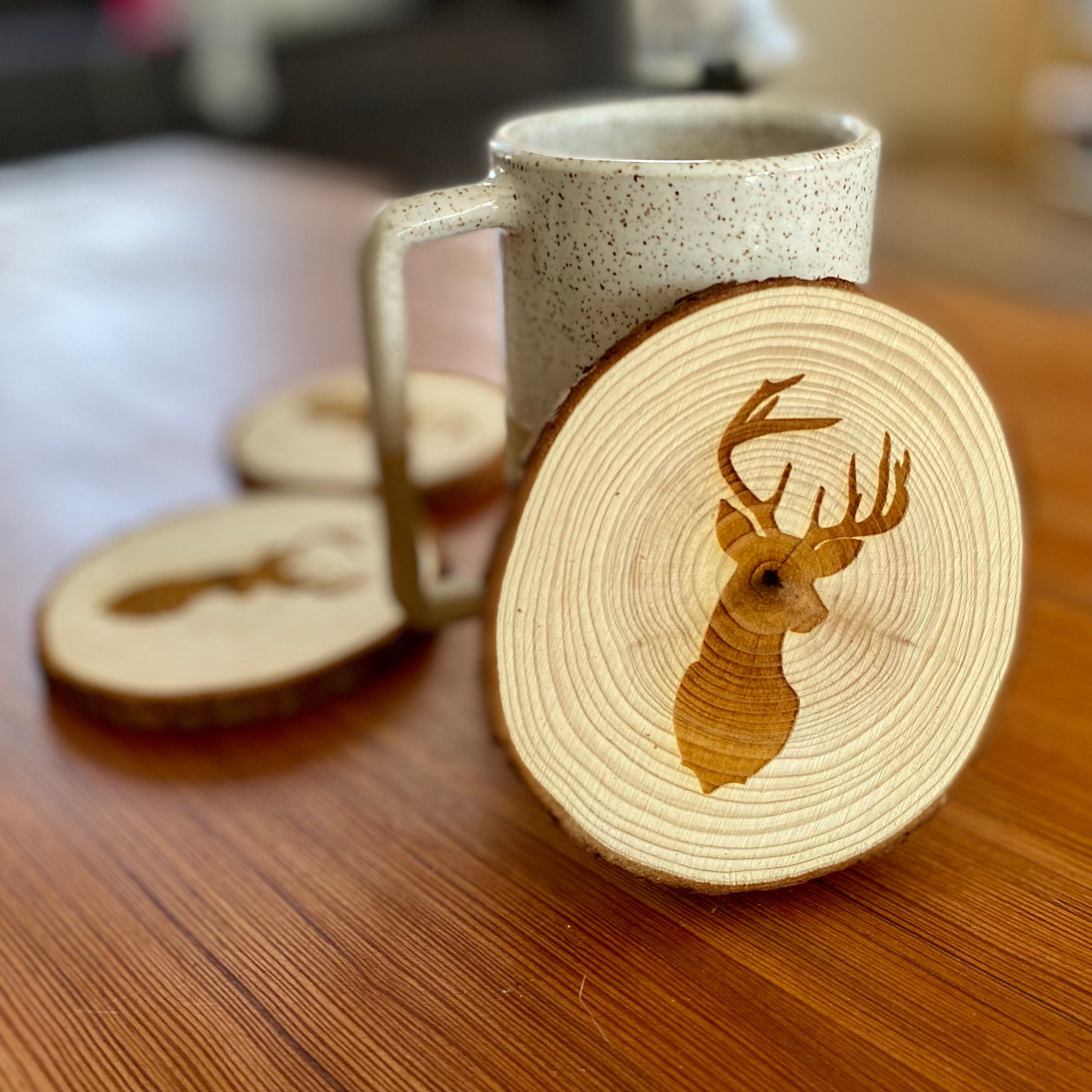 A set of four laser engraved wood coasters featuring a deer head silhouette, showcasing their natural wood finish and unique design.