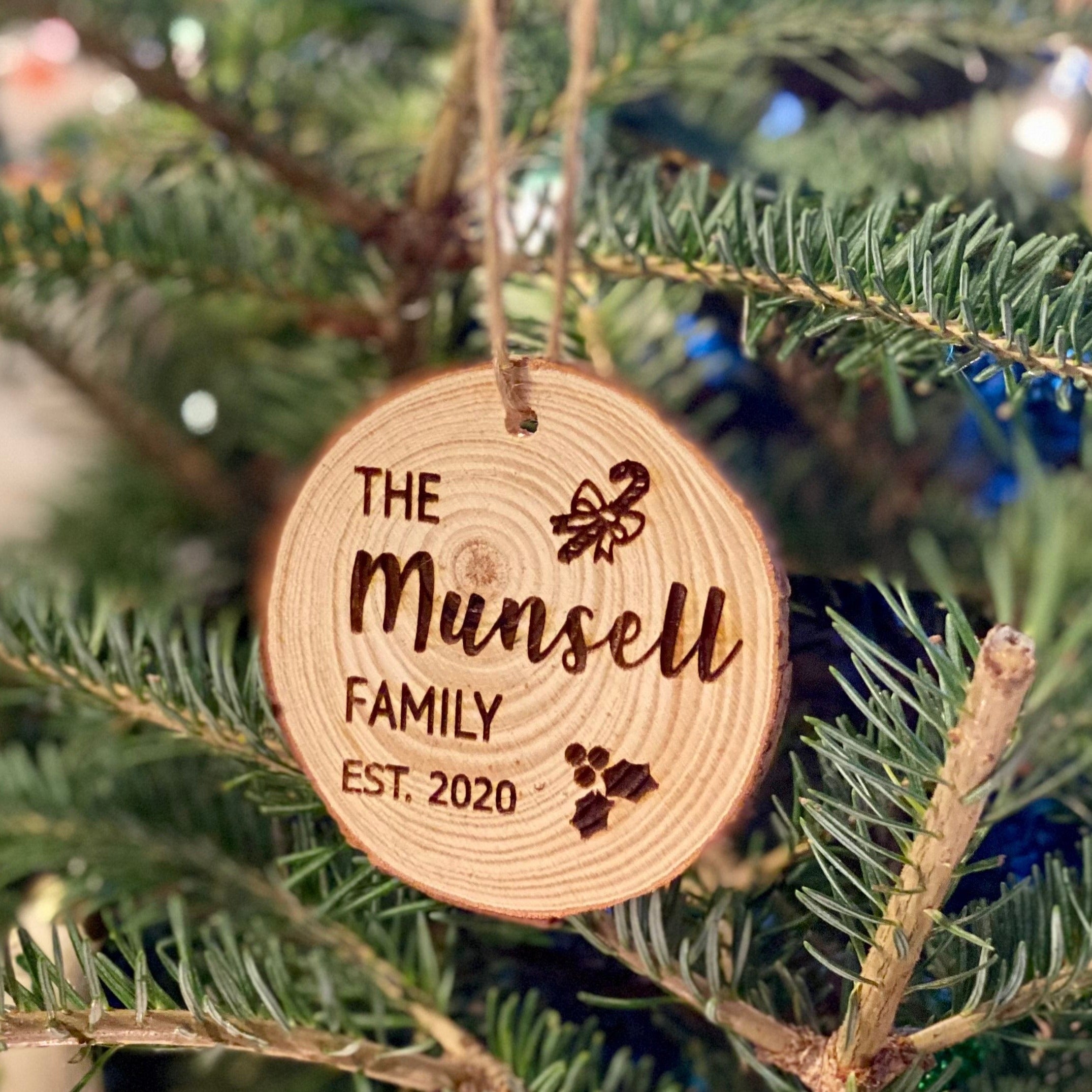 Engraved wood slice ornament featuring family name and year, decorated with candy cane and holly accents.