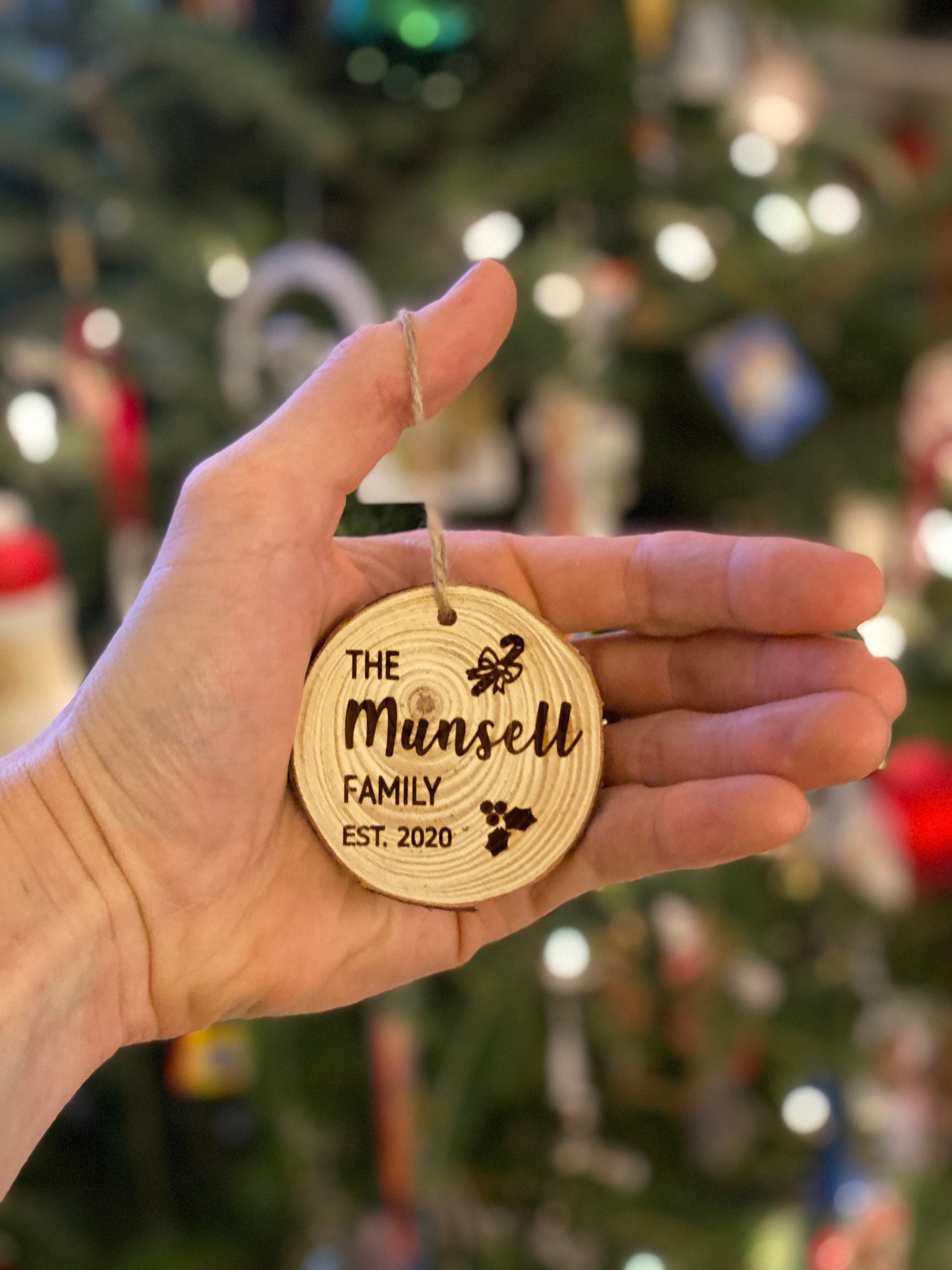 Engraved wood slice ornament featuring family name and year, decorated with candy cane and holly accents.