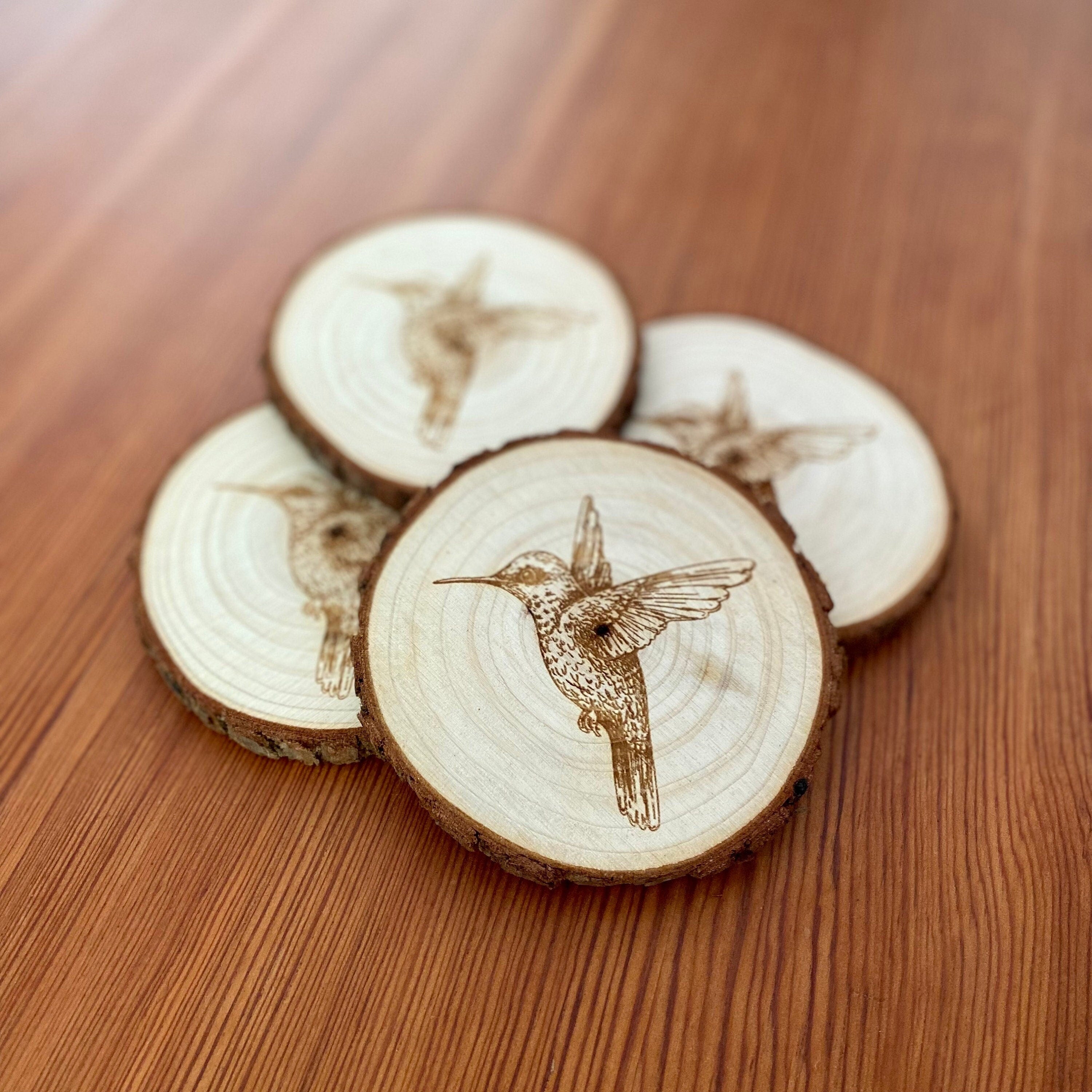 Set of four laser engraved wood coasters featuring intricate hummingbird designs, showcasing natural wood texture.