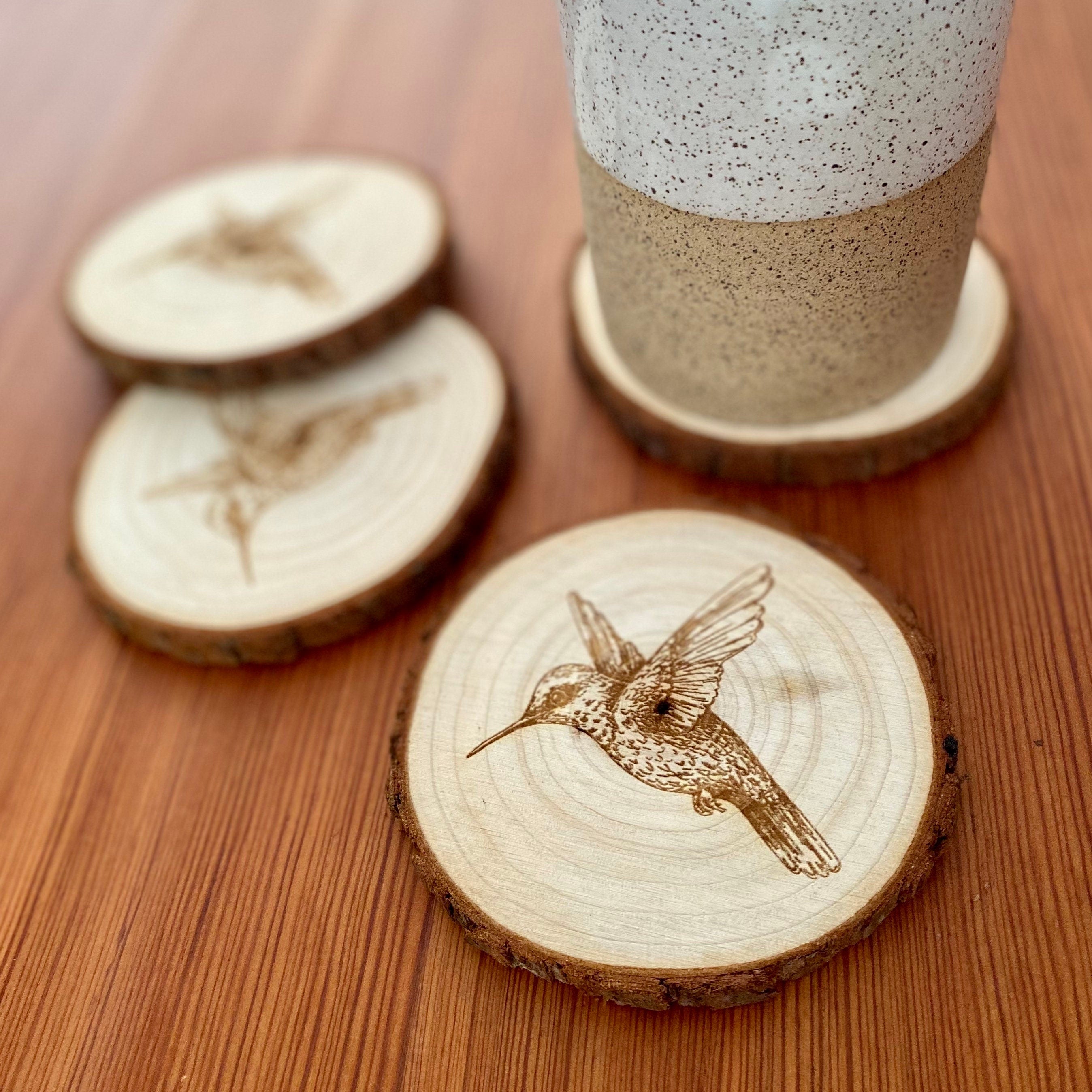 Set of four laser engraved wood coasters featuring intricate hummingbird designs, showcasing natural wood texture.