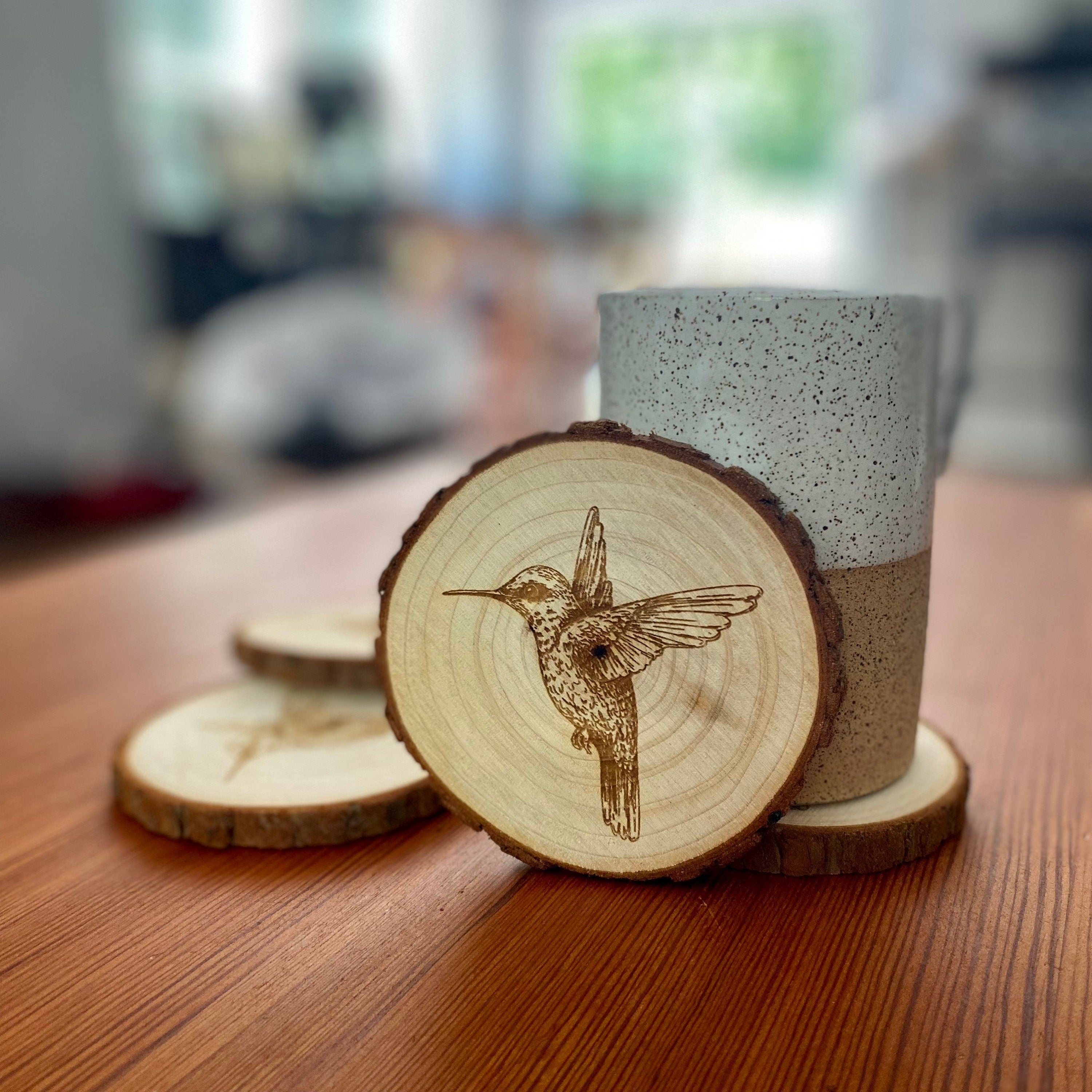 Set of four laser engraved wood coasters featuring intricate hummingbird designs, showcasing natural wood texture.