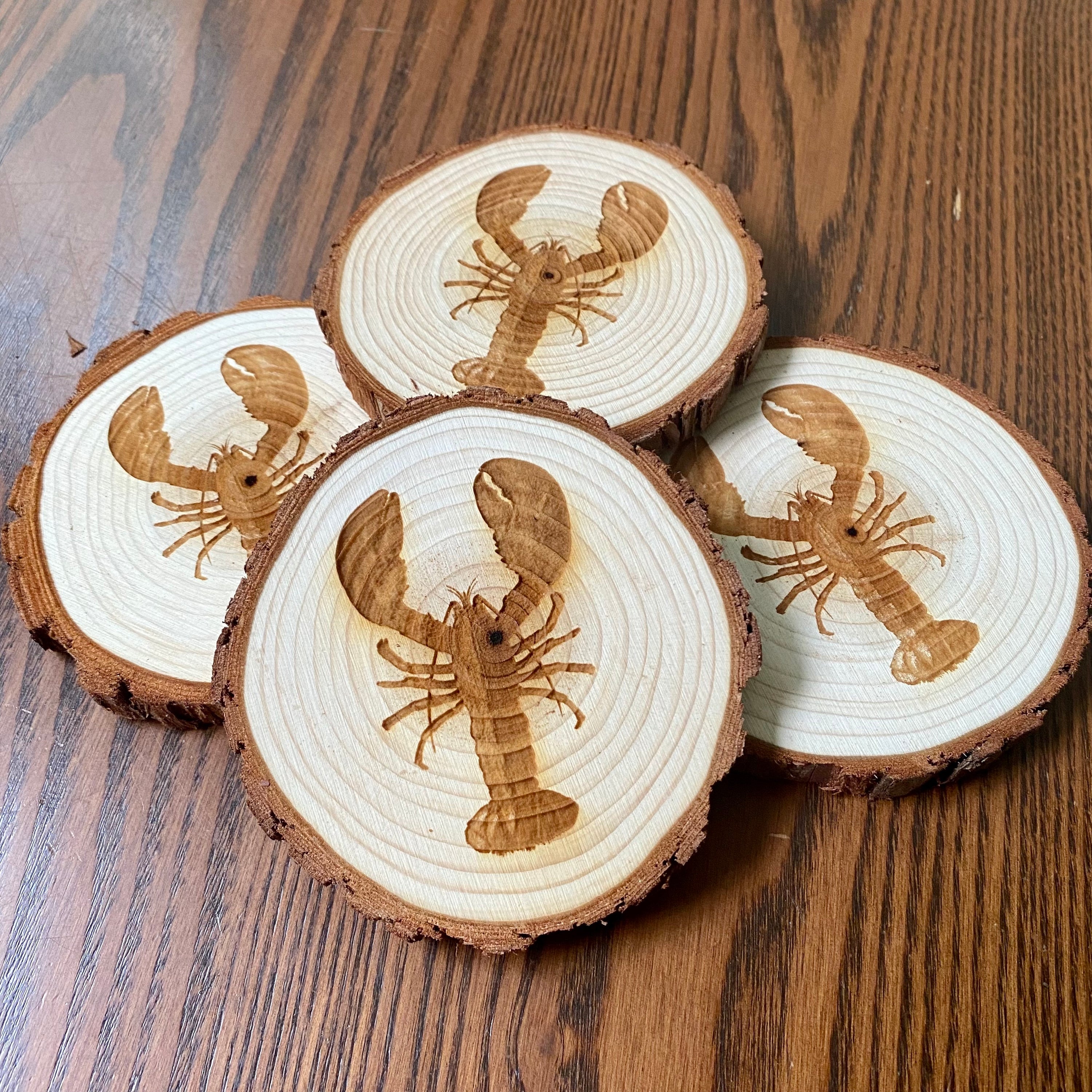 A set of four laser engraved wood coasters featuring intricate lobster designs, showcasing their natural wood finish and unique textures.