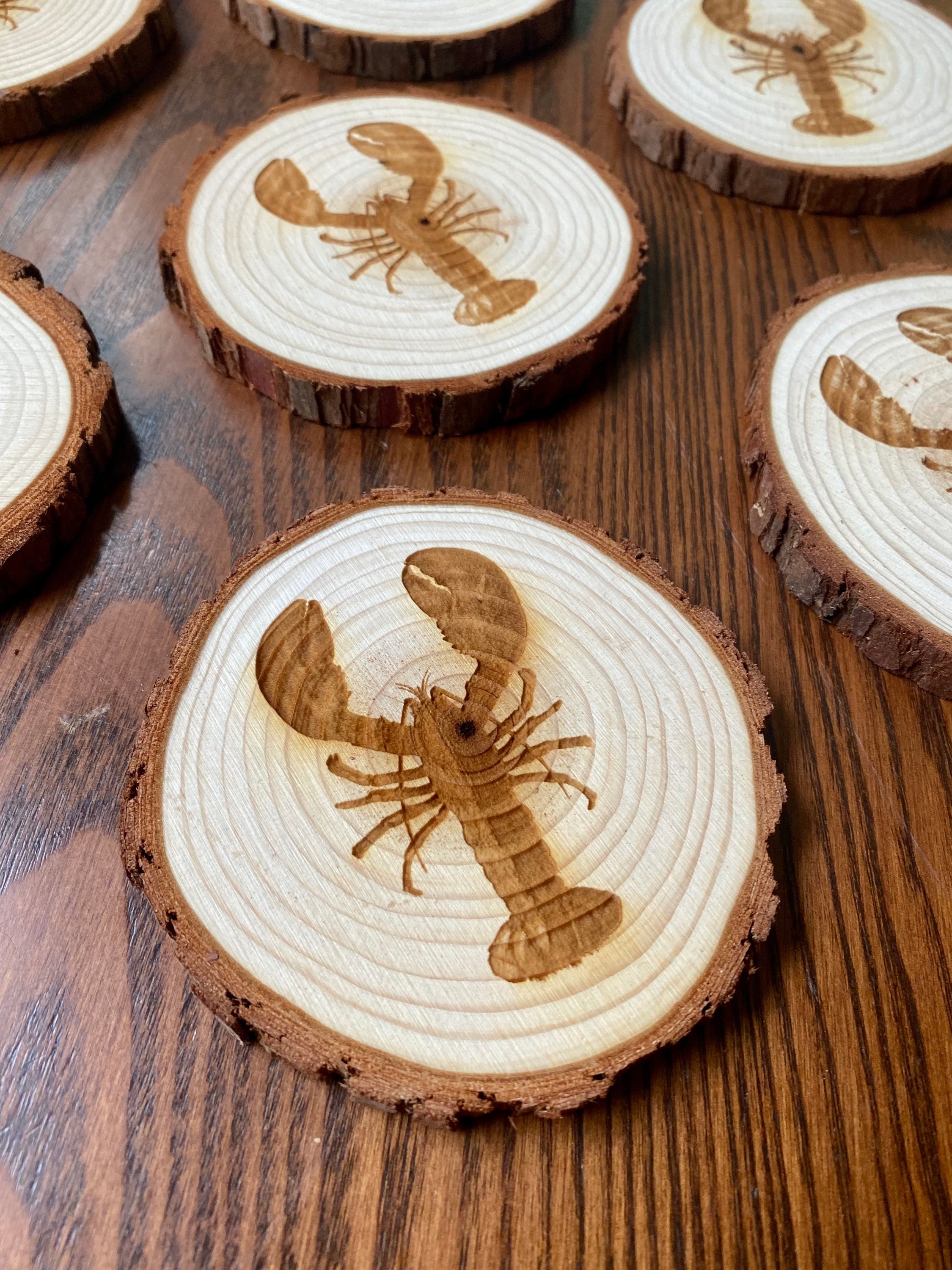 A set of four laser engraved wood coasters featuring intricate lobster designs, showcasing their natural wood finish and unique textures.