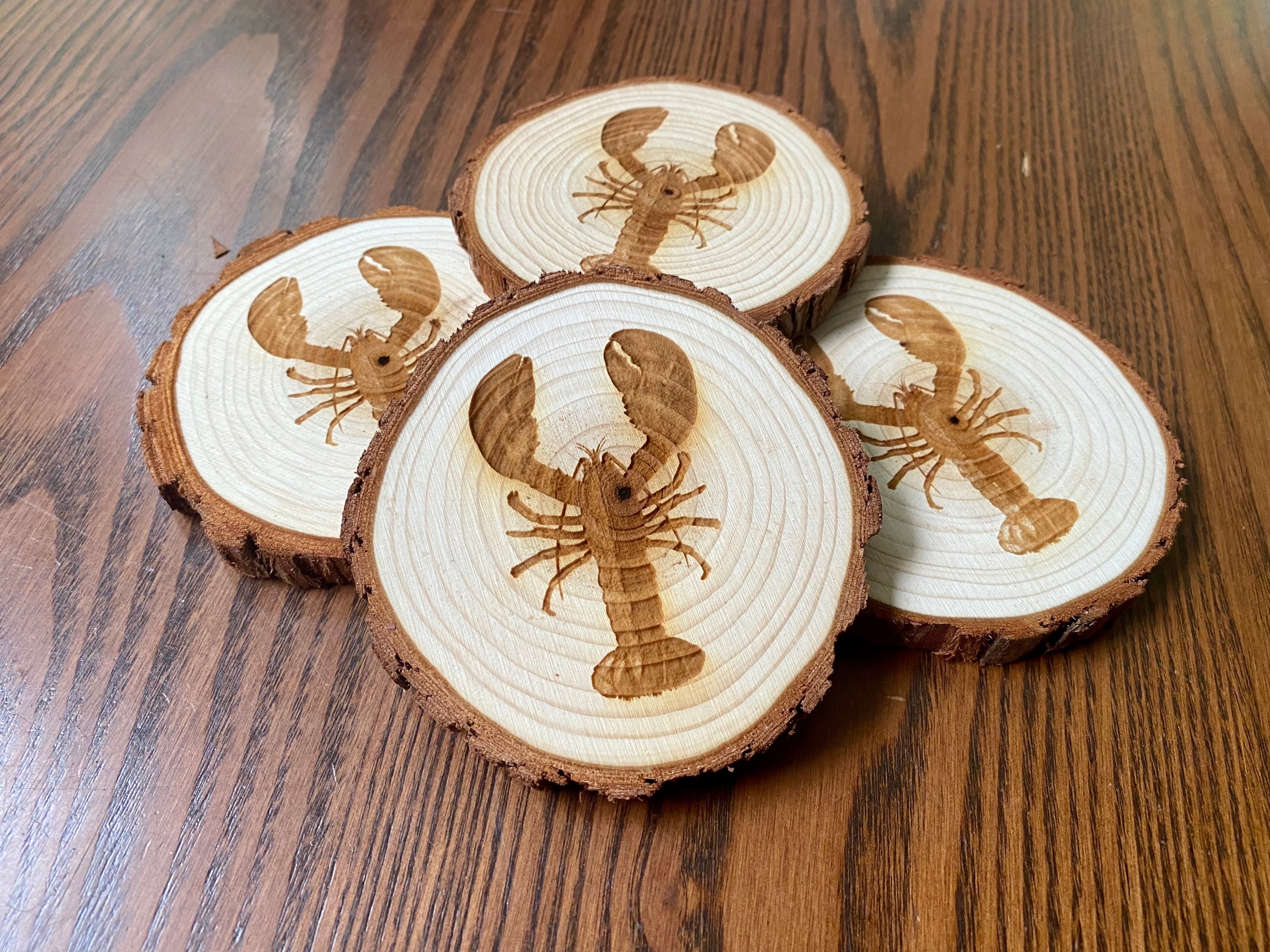 A set of four laser engraved wood coasters featuring intricate lobster designs, showcasing their natural wood finish and unique textures.