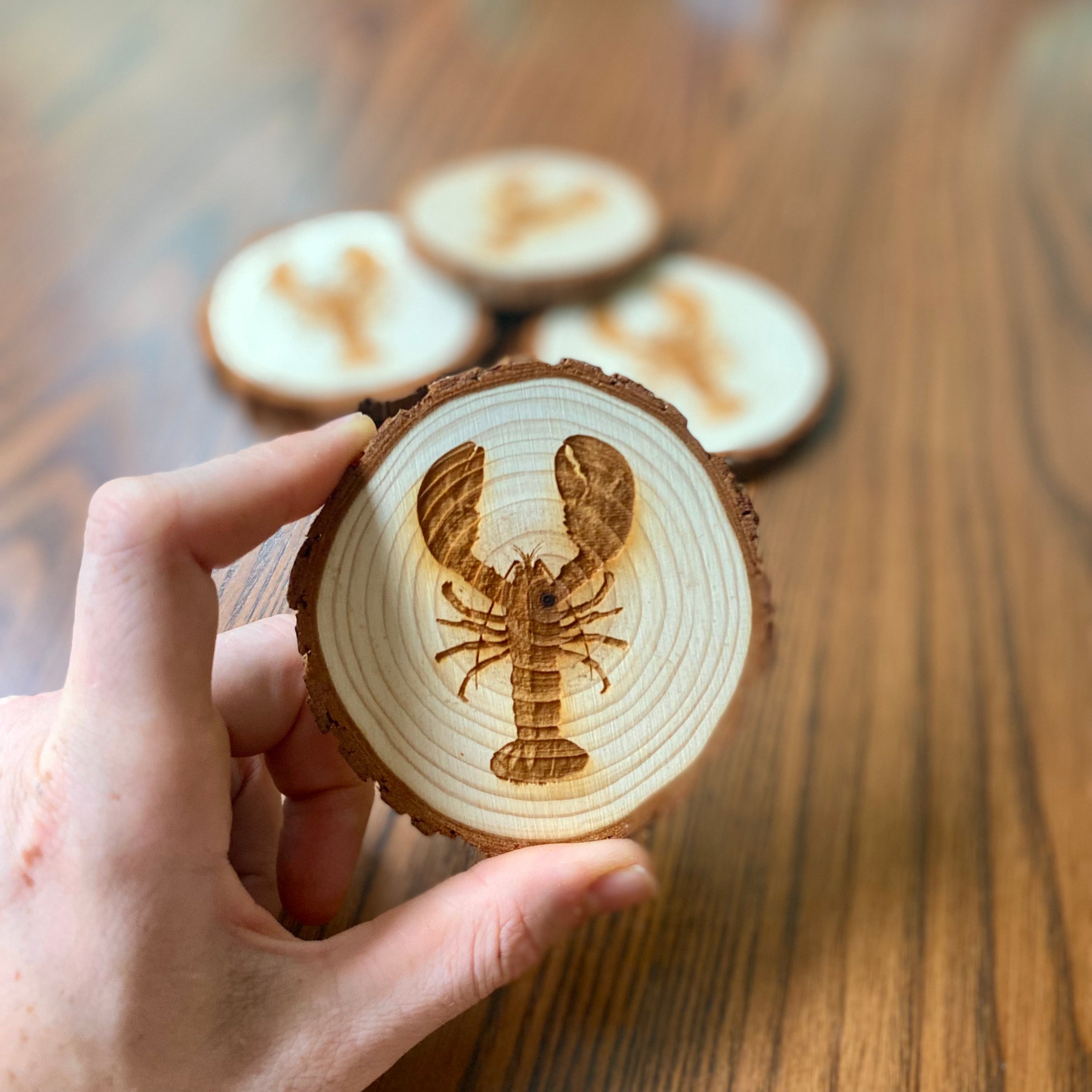 A set of four laser engraved wood coasters featuring intricate lobster designs, showcasing their natural wood finish and unique textures.