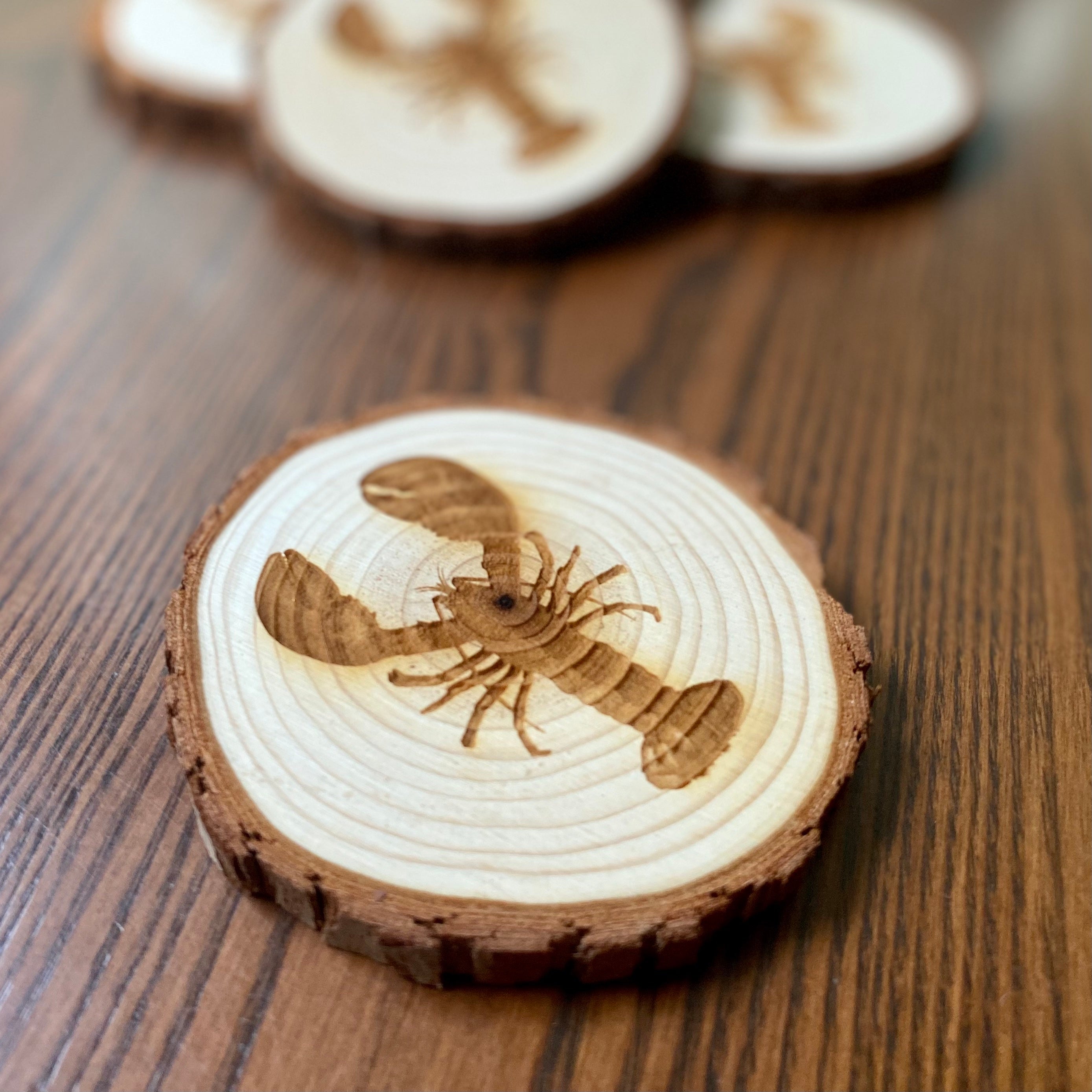 A set of four laser engraved wood coasters featuring intricate lobster designs, showcasing their natural wood finish and unique textures.