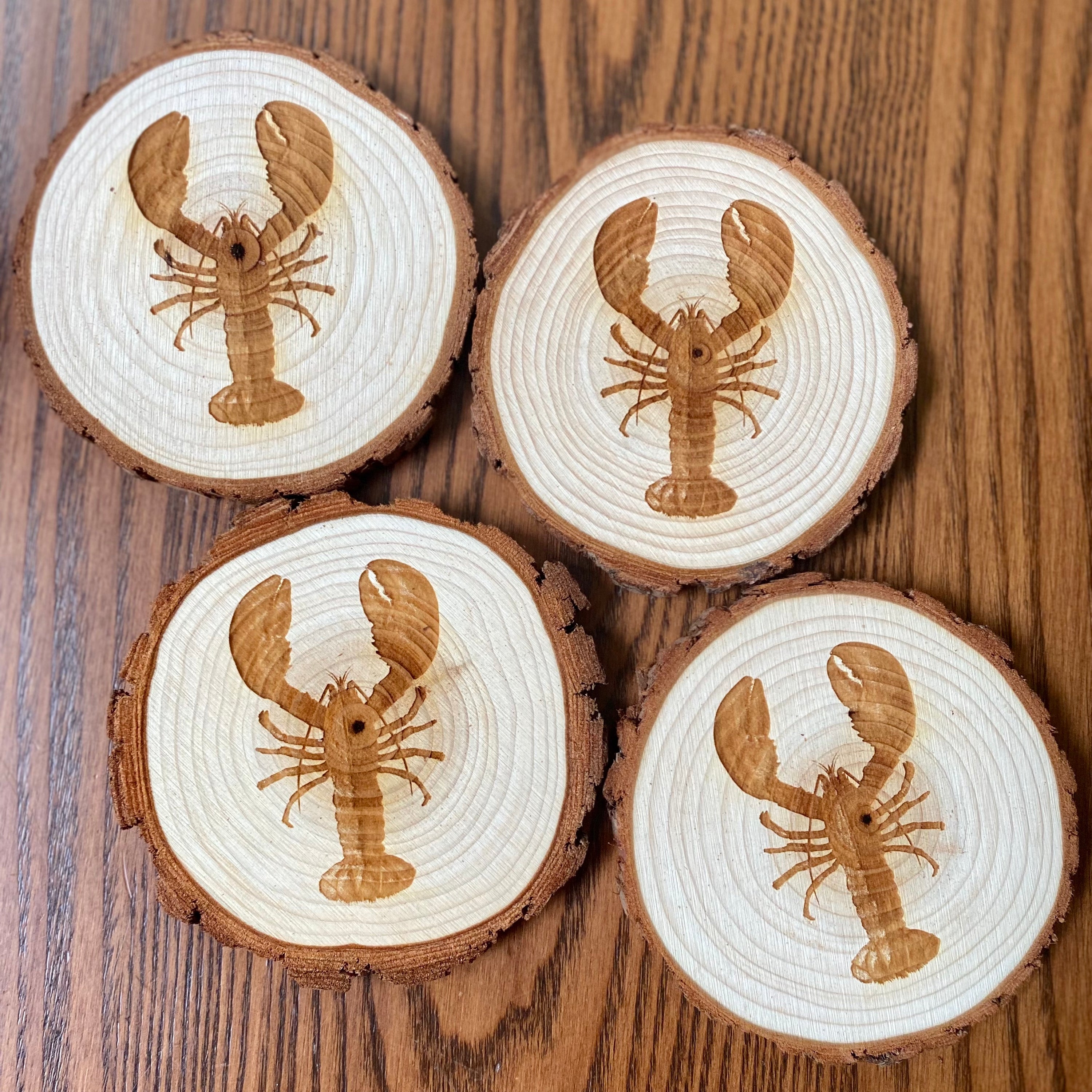 A set of four laser engraved wood coasters featuring intricate lobster designs, showcasing their natural wood finish and unique textures.