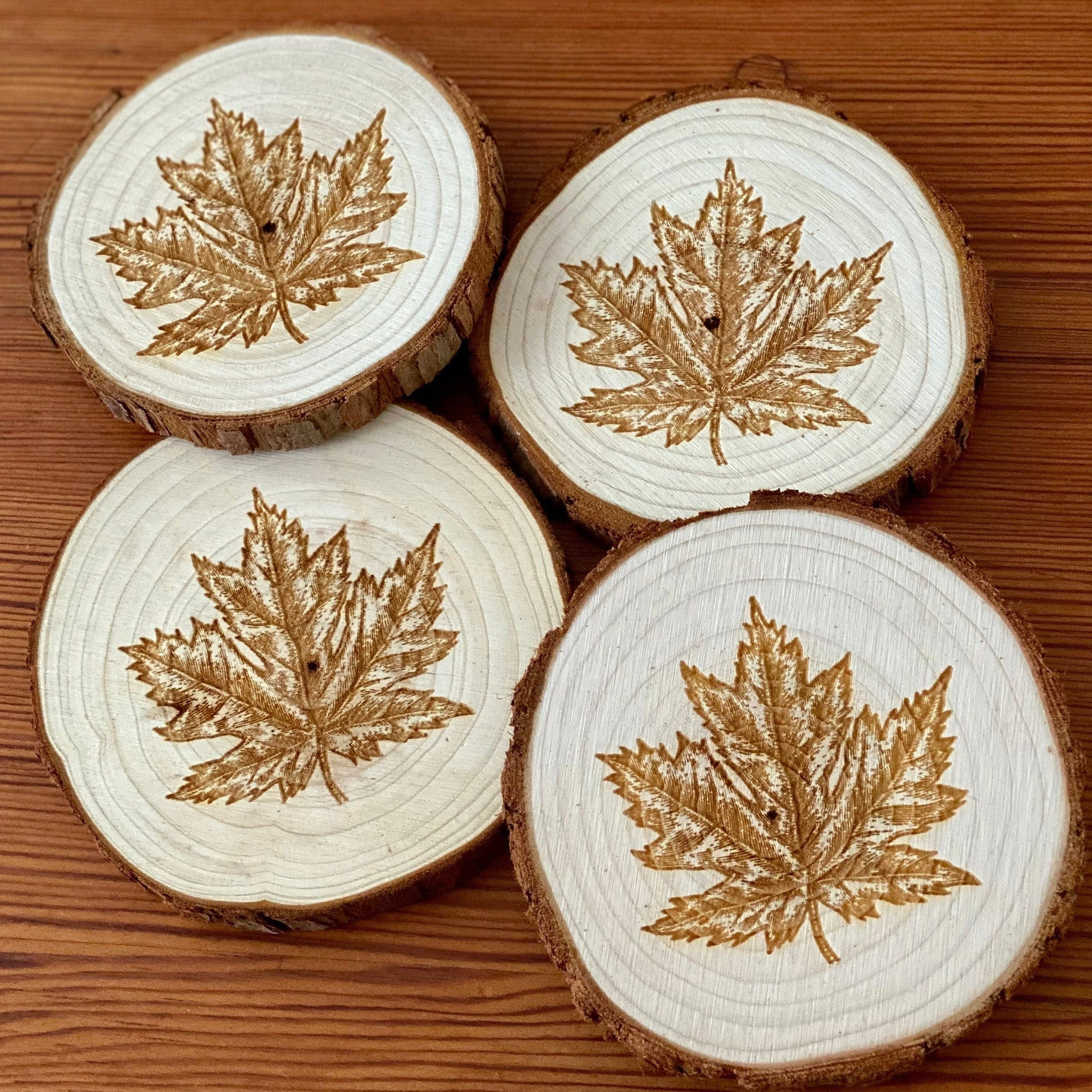 A set of four wooden coasters featuring intricate maple leaf engravings, showcasing their natural wood finish and unique design.