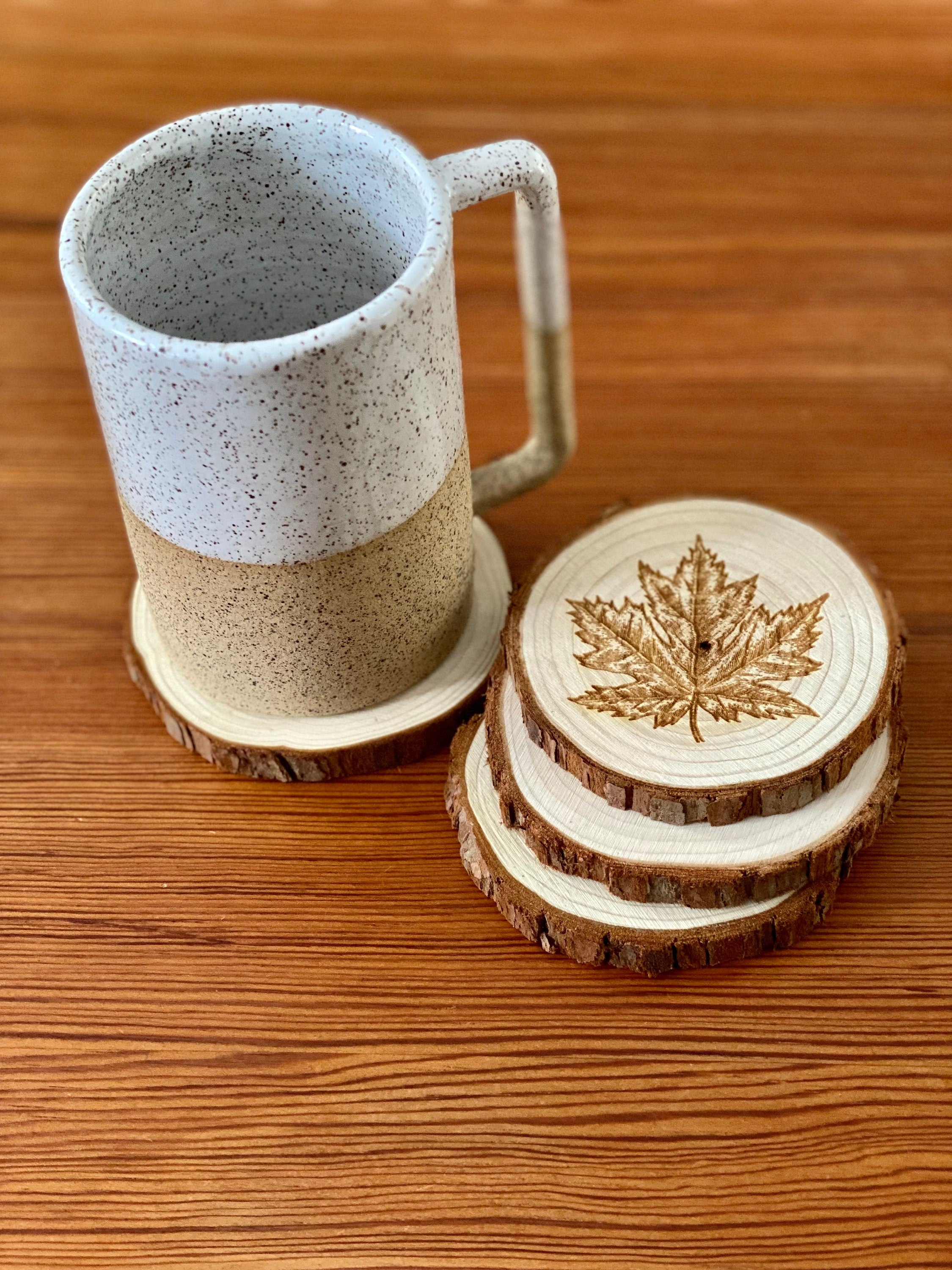 A set of four wooden coasters featuring intricate maple leaf engravings, showcasing their natural wood finish and unique design.