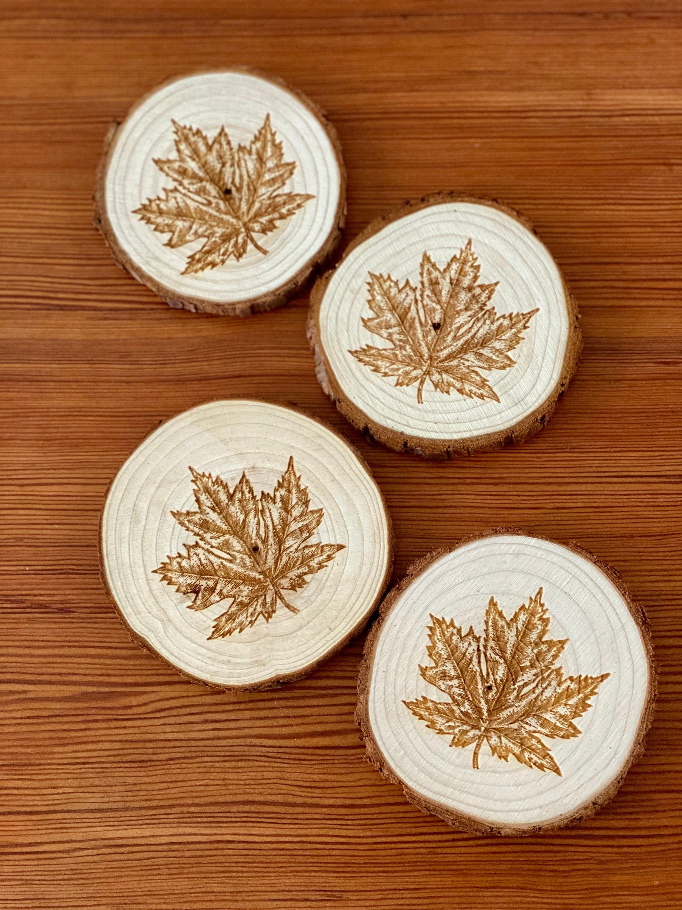 A set of four wooden coasters featuring intricate maple leaf engravings, showcasing their natural wood finish and unique design.