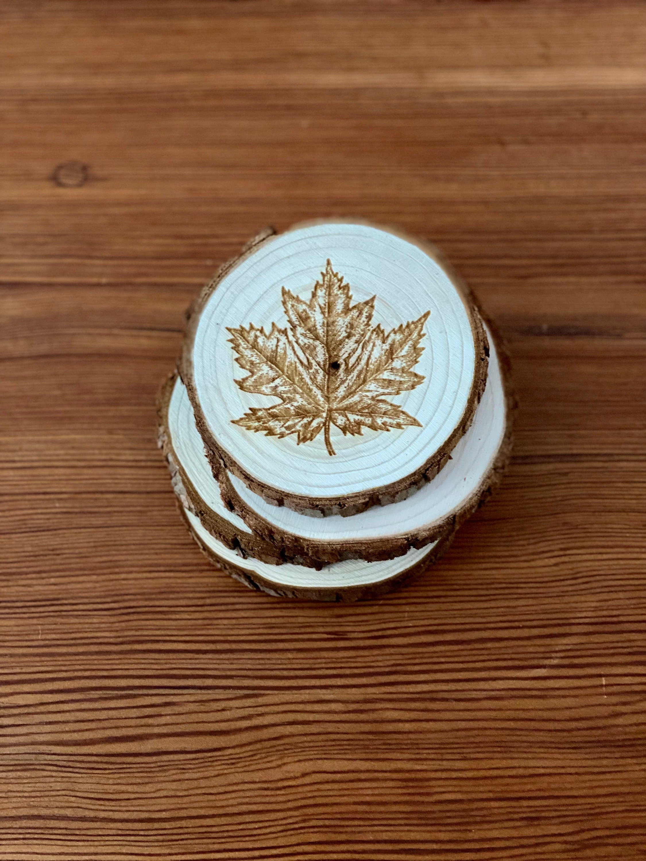 A set of four wooden coasters featuring intricate maple leaf engravings, showcasing their natural wood finish and unique design.