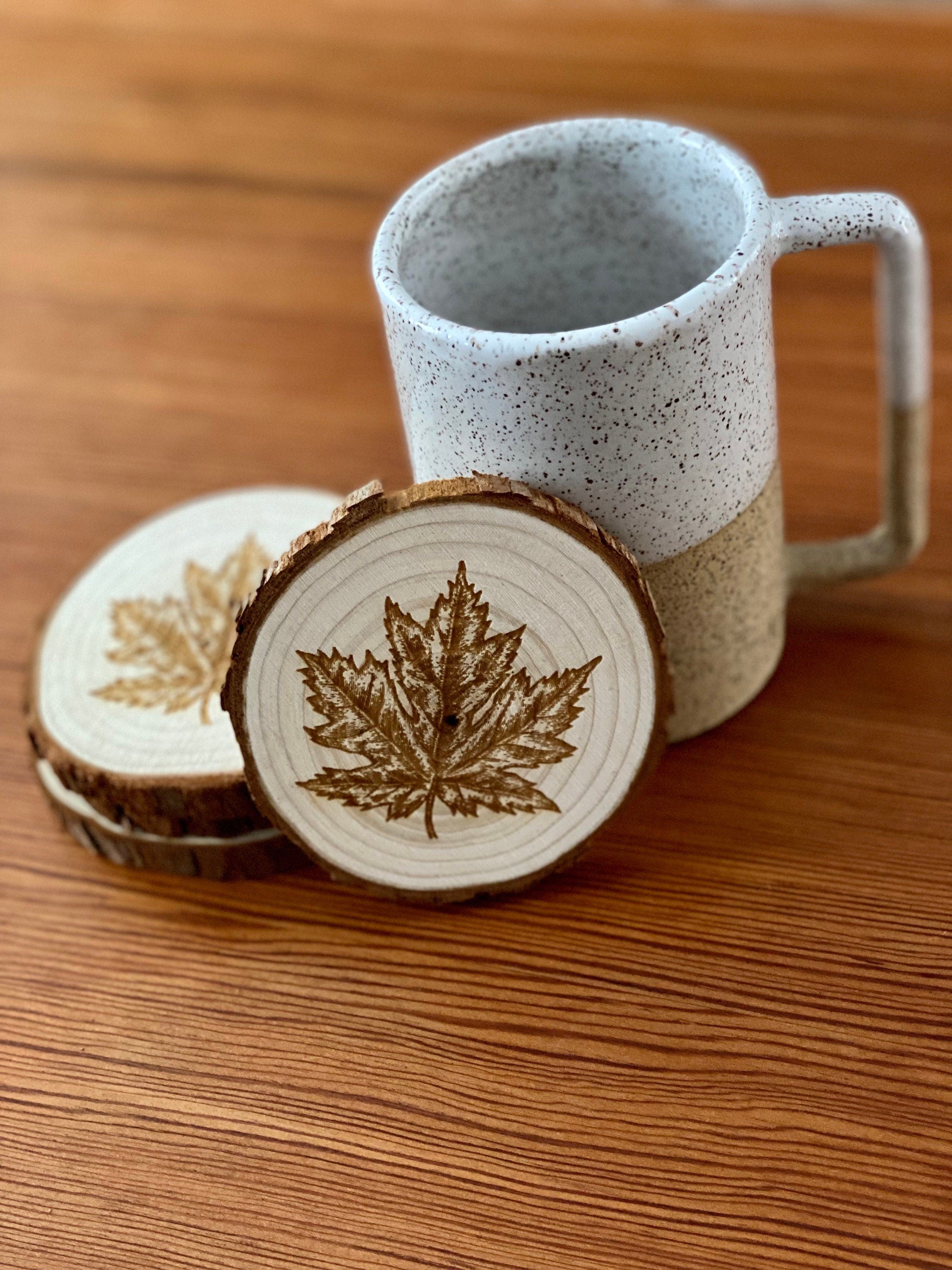 A set of four wooden coasters featuring intricate maple leaf engravings, showcasing their natural wood finish and unique design.