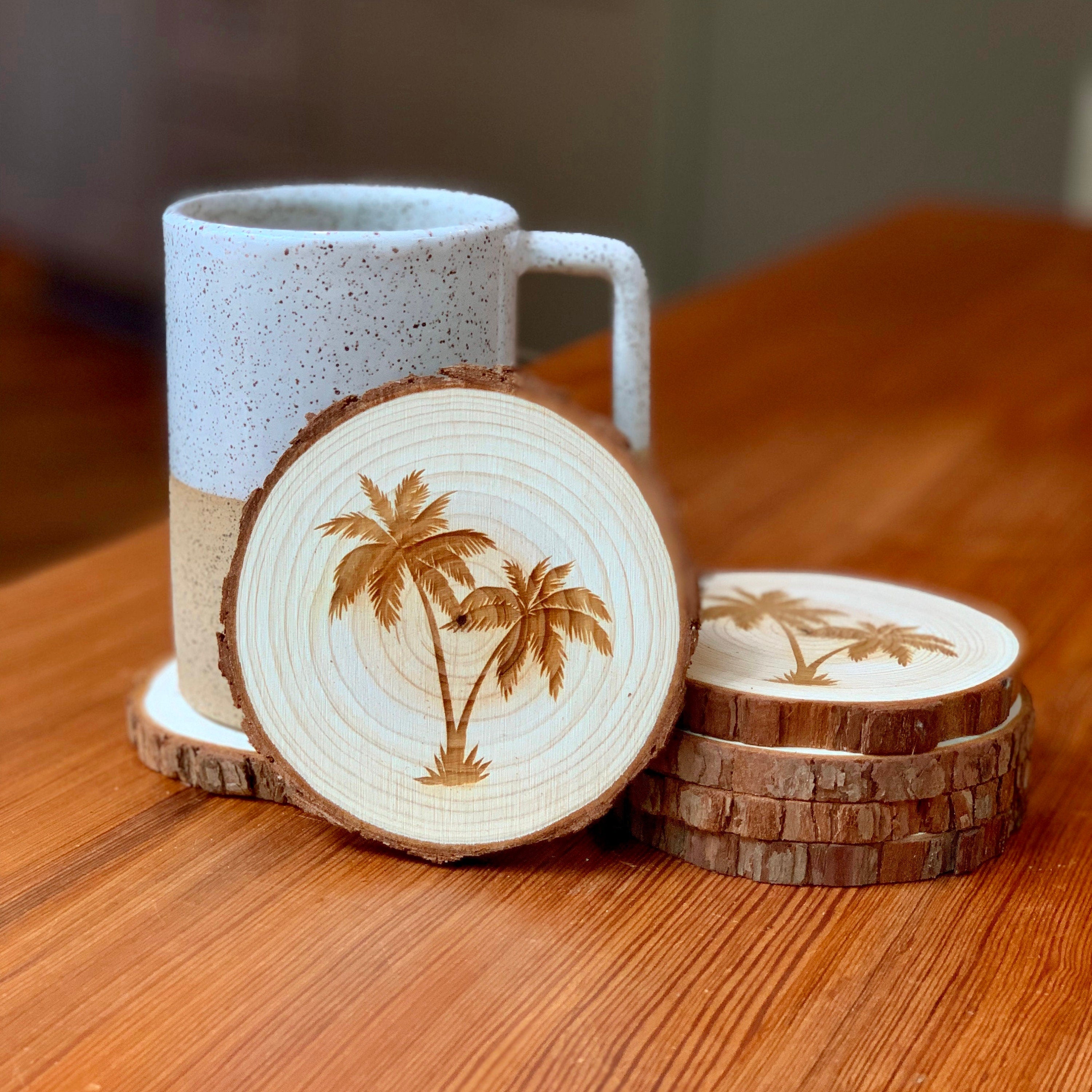 A set of four palm tree engraved wood coasters on a rustic wooden table, showcasing their natural finish and intricate designs.