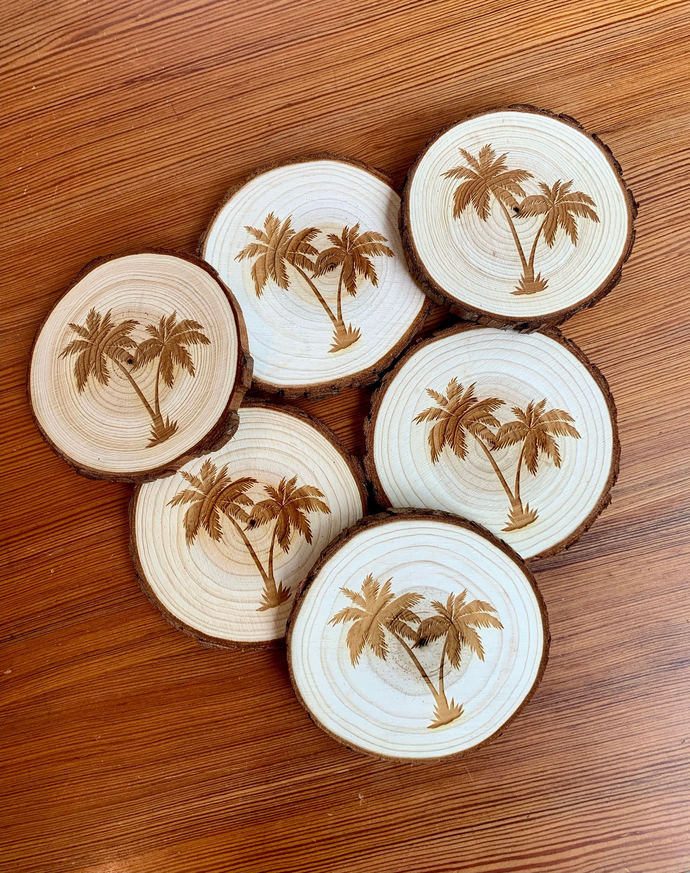 A set of four palm tree engraved wood coasters on a rustic wooden table, showcasing their natural finish and intricate designs.