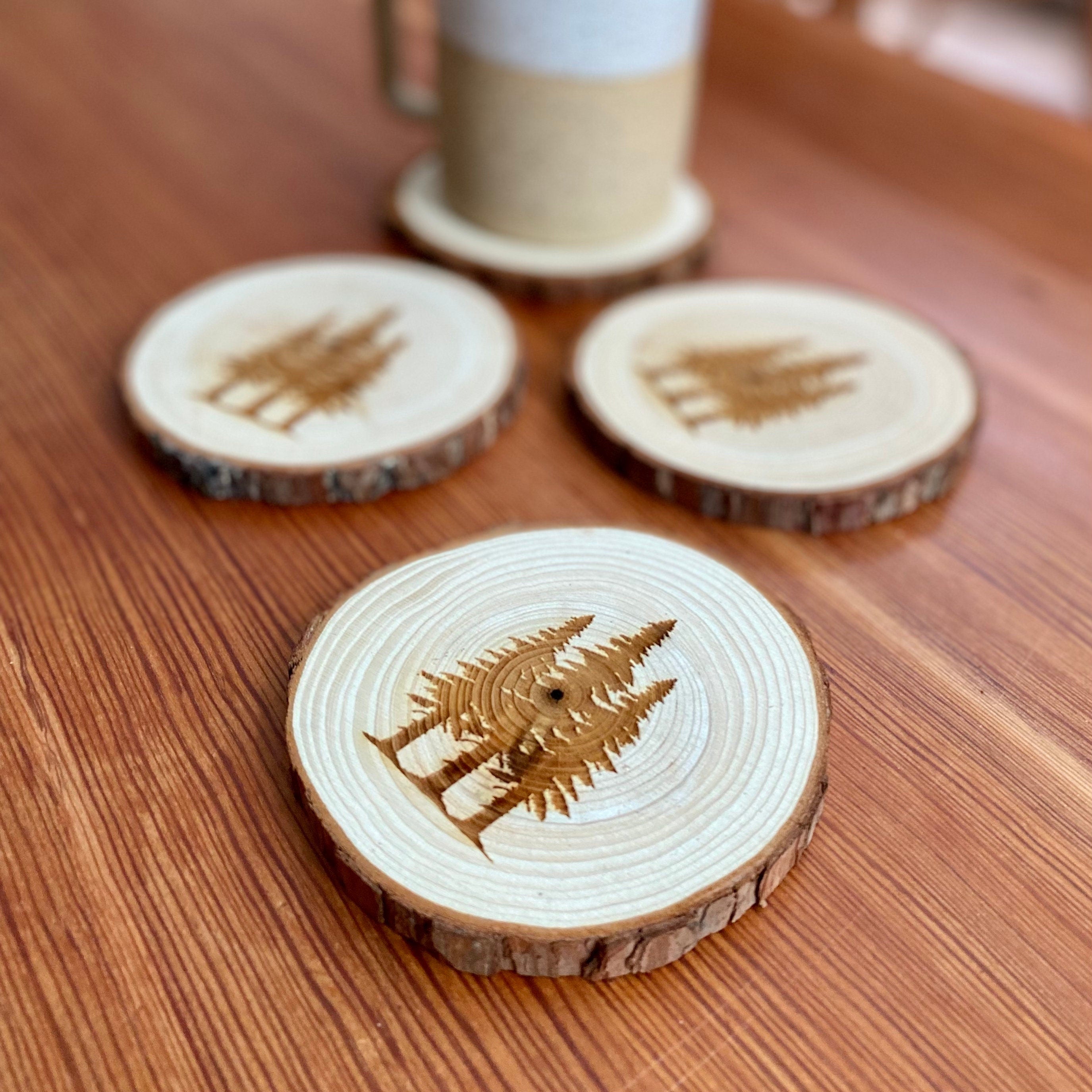 A set of four pine tree engraved wood coasters, showcasing intricate designs on a rustic wood surface, ideal for home decor.