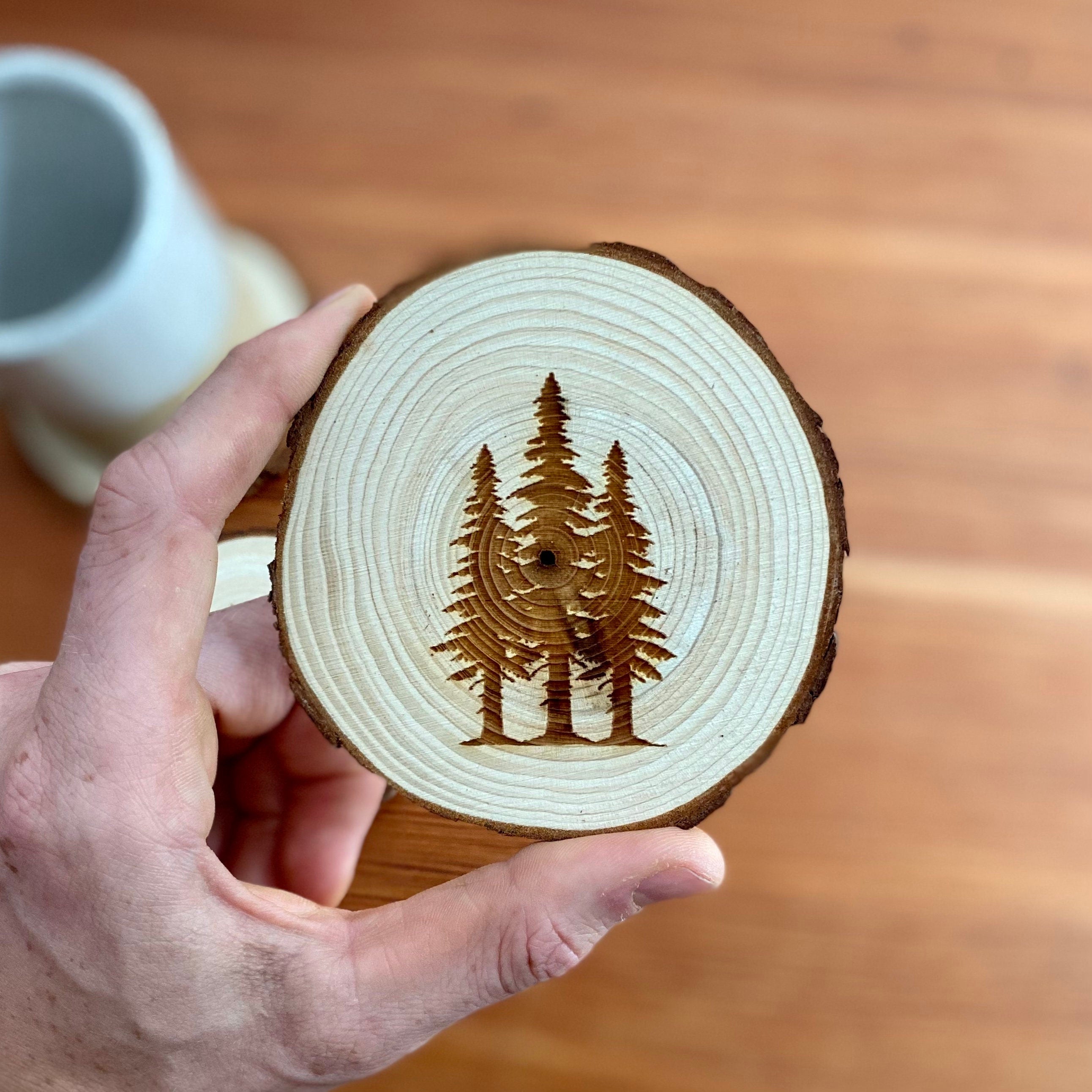 A set of four pine tree engraved wood coasters, showcasing intricate designs on a rustic wood surface, ideal for home decor.