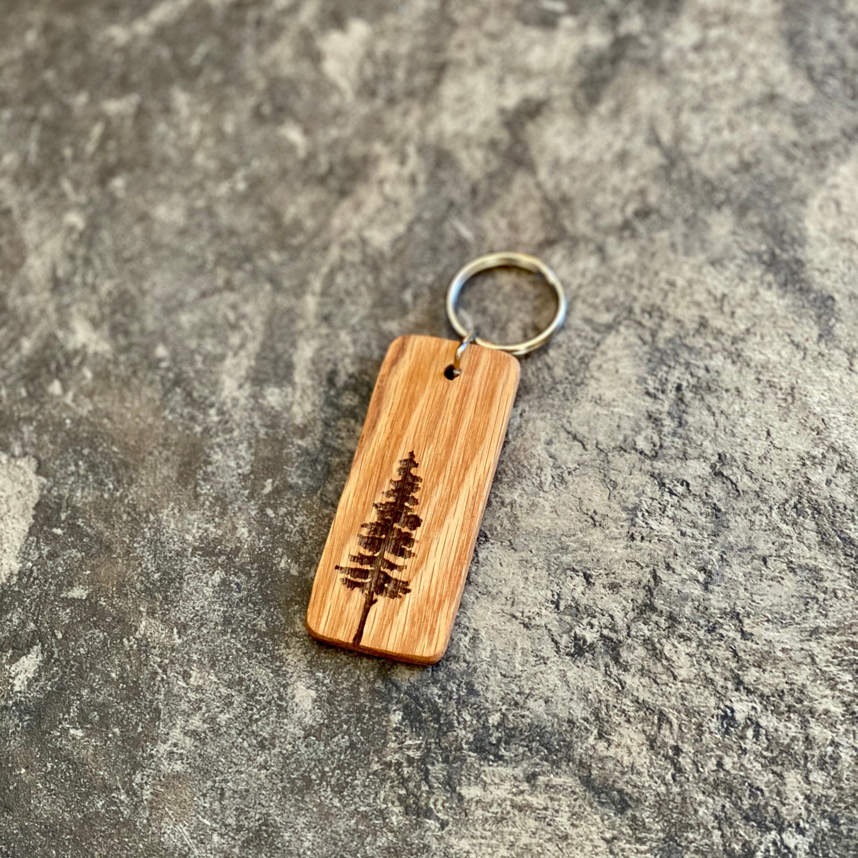 A rustic Pine Tree Engraved Wood Keychain made from solid hardwood oak, featuring a detailed pine tree silhouette and space for personalized text.