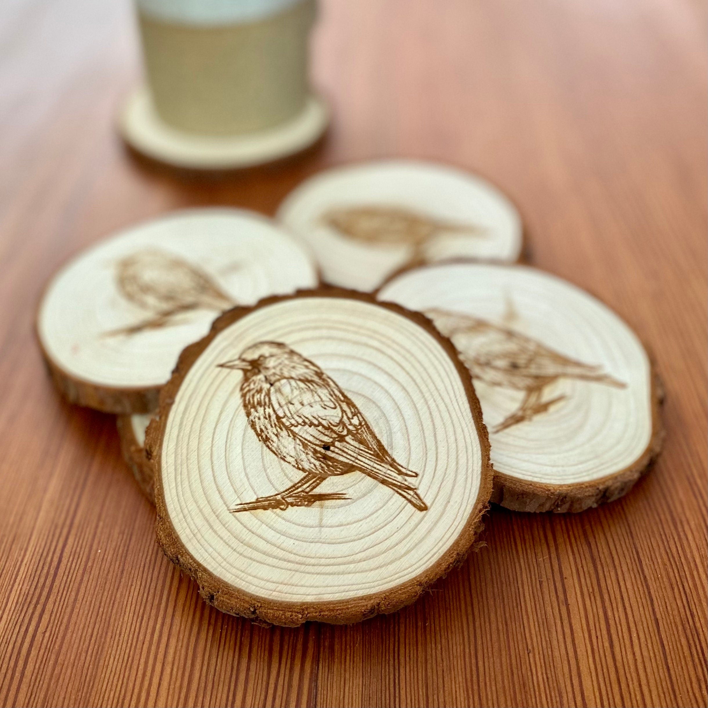 A set of four laser engraved wood coasters featuring starling bird illustrations, showcasing their natural wood finish and intricate designs.