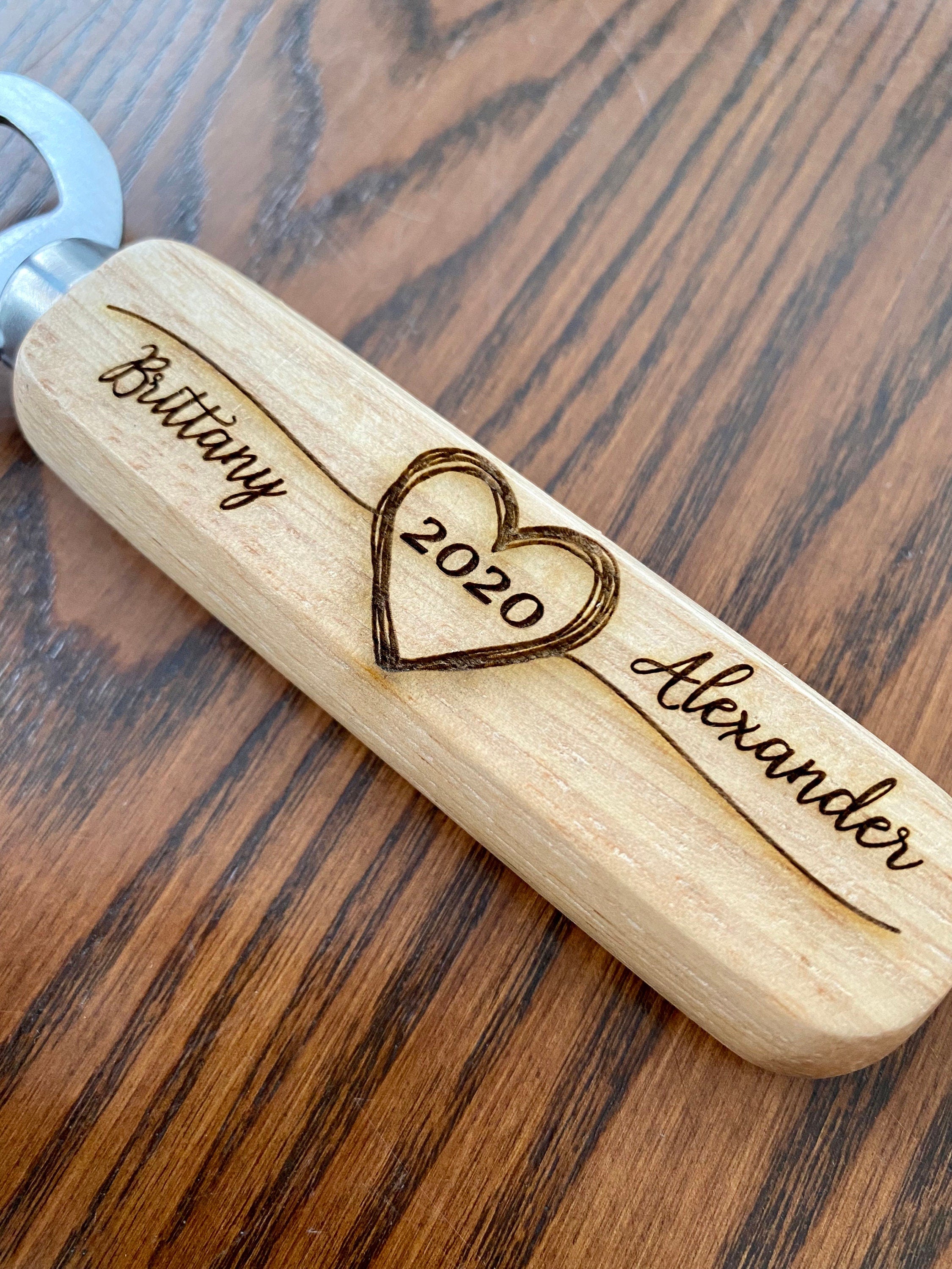 Personalized wooden bottle opener with engraved names and heart design, perfect for rustic wedding favors.