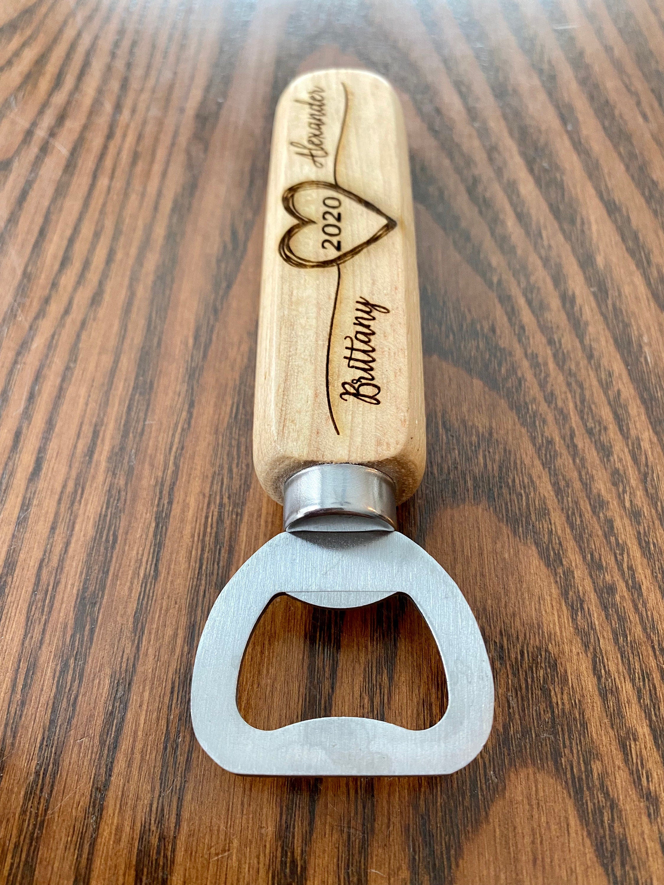 Personalized wooden bottle opener with engraved names and heart design, perfect for rustic wedding favors.