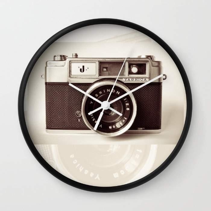 A stylish Camera Wall Clock featuring a high-impact plexiglass face, available in black or white frames, with customizable hands and a sleek design.