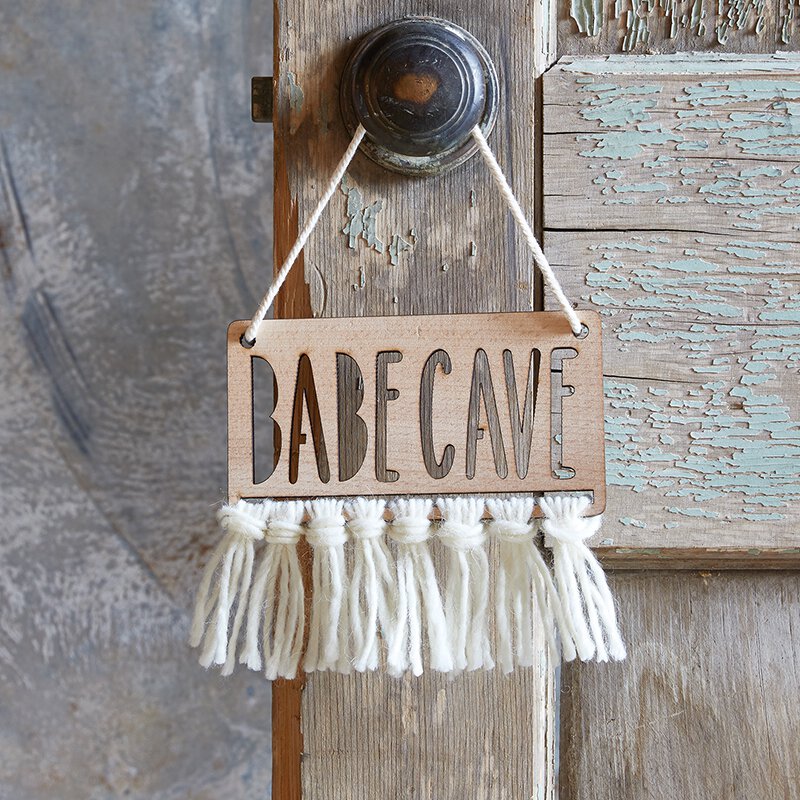 Babe Cave Wood Door Sign made from natural beech wood with humorous text and fringe embellishment, hanging on a wall.