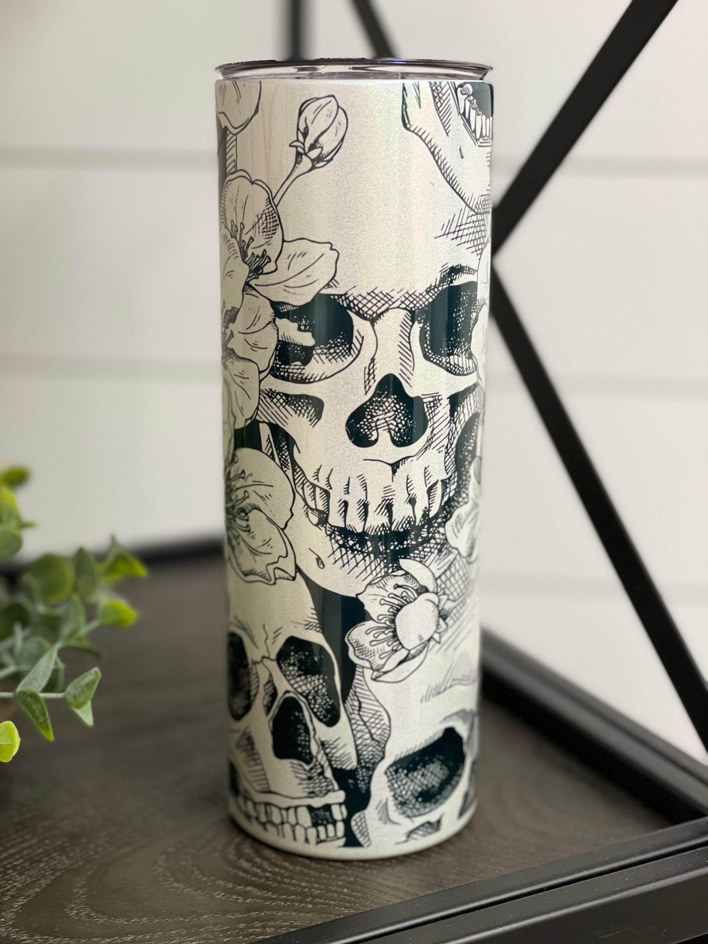 A vibrant 20oz skinny tumbler featuring a floral skull design with a shimmering rainbow effect, perfect for drinks.