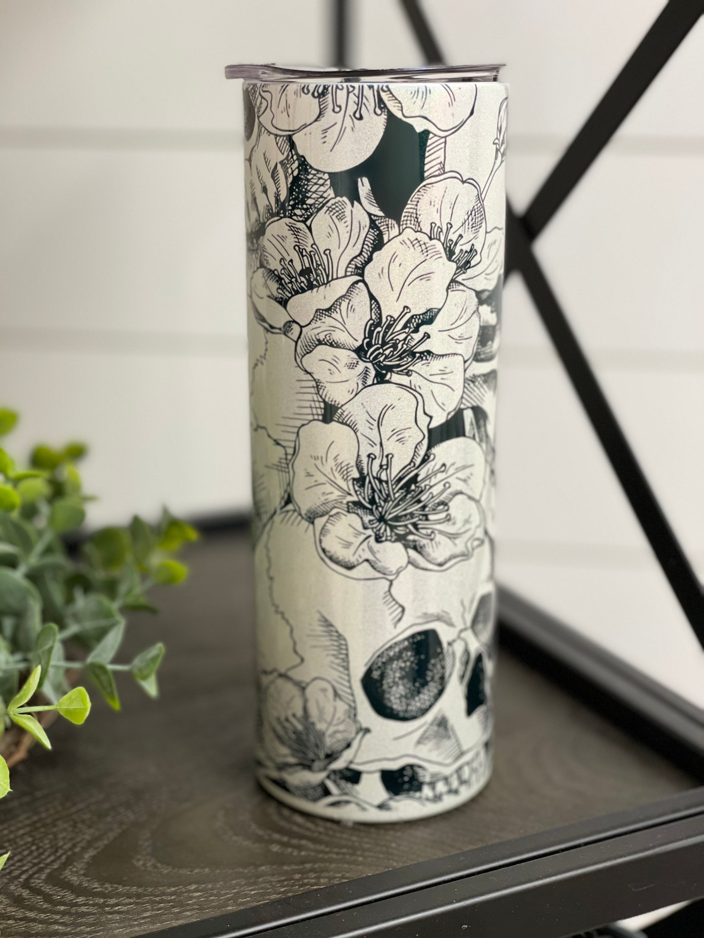 A vibrant 20oz skinny tumbler featuring a floral skull design with a shimmering rainbow effect, perfect for drinks.