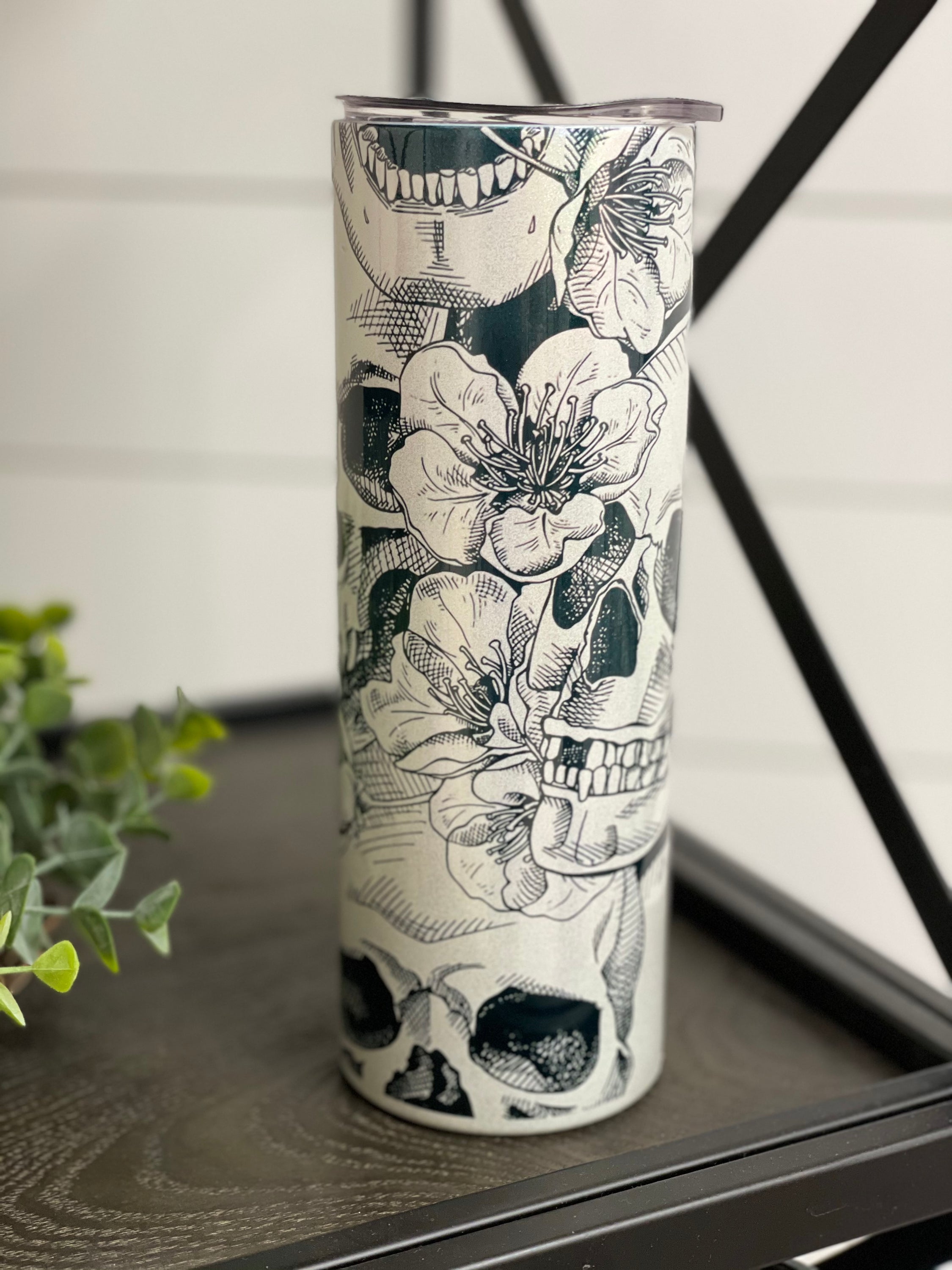 A vibrant 20oz skinny tumbler featuring a floral skull design with a shimmering rainbow effect, perfect for drinks.