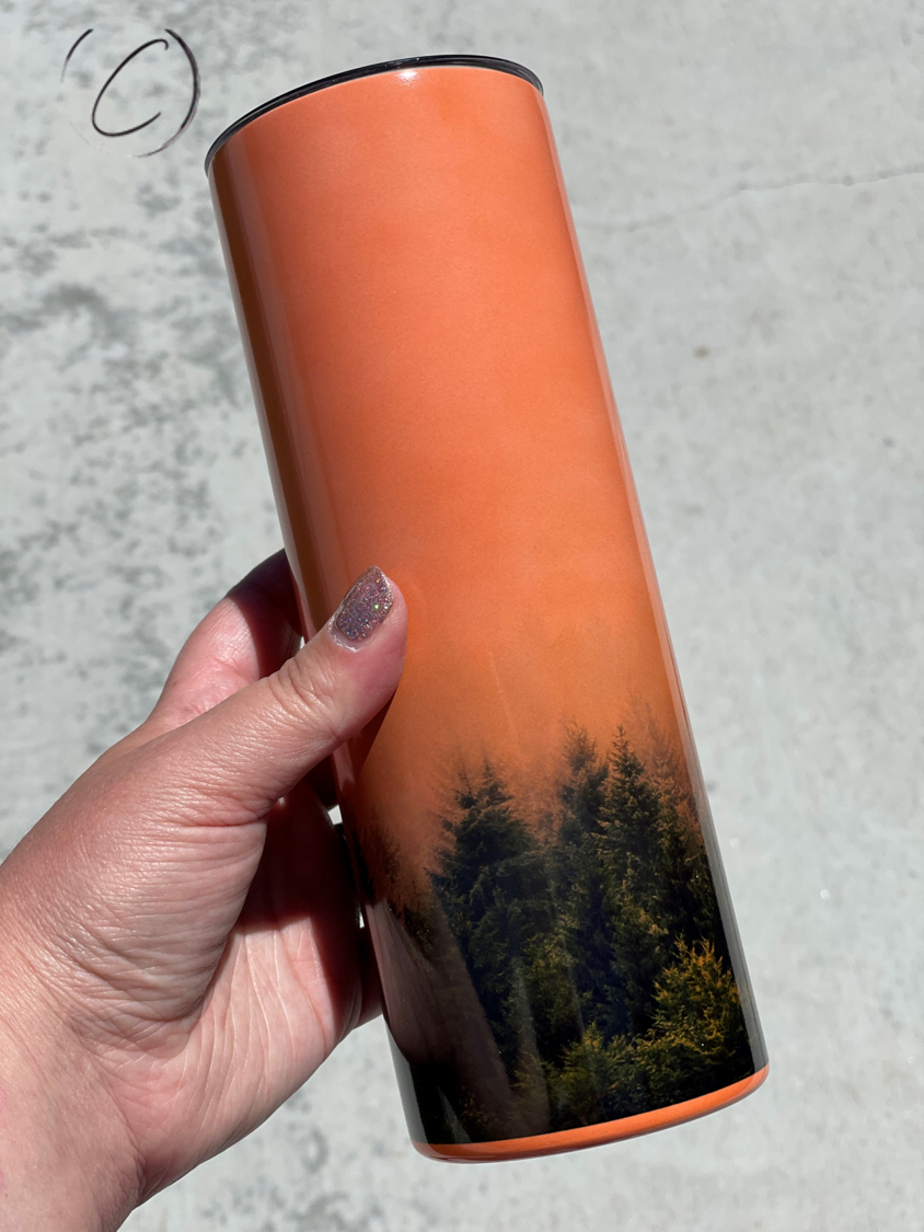 Forest Fog 20oz UV Orange Skinny Tumbler showcasing its vibrant color-changing design in sunlight, complete with a reusable straw.