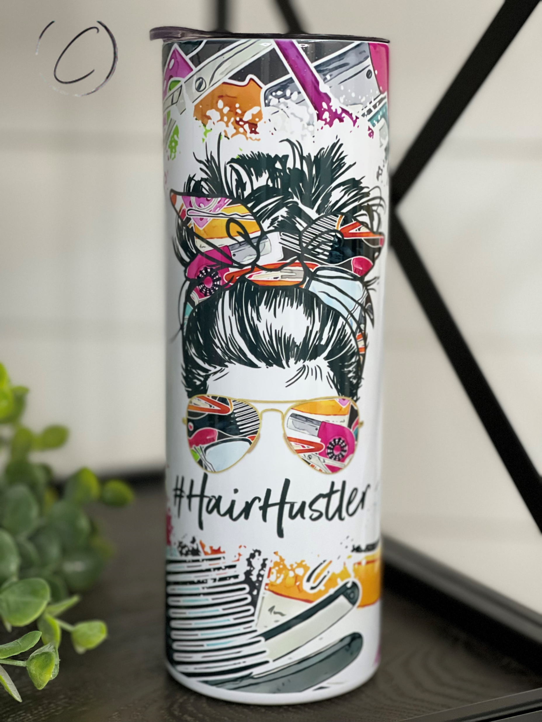 A stylish #HairHuslter 20oz skinny tumbler featuring a vibrant full wrap design, complete with a reusable straw.