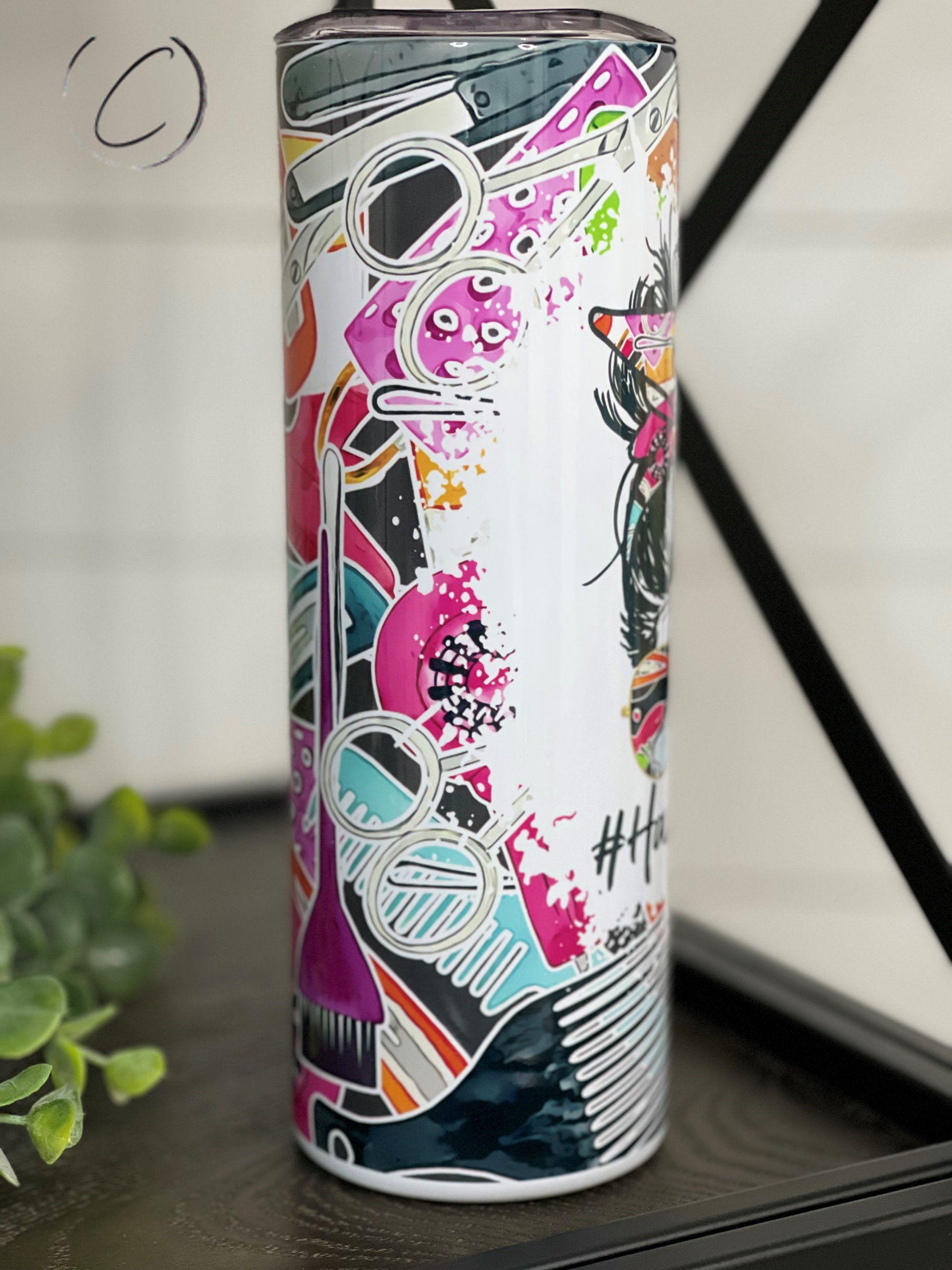 A stylish #HairHuslter 20oz skinny tumbler featuring a vibrant full wrap design, complete with a reusable straw.