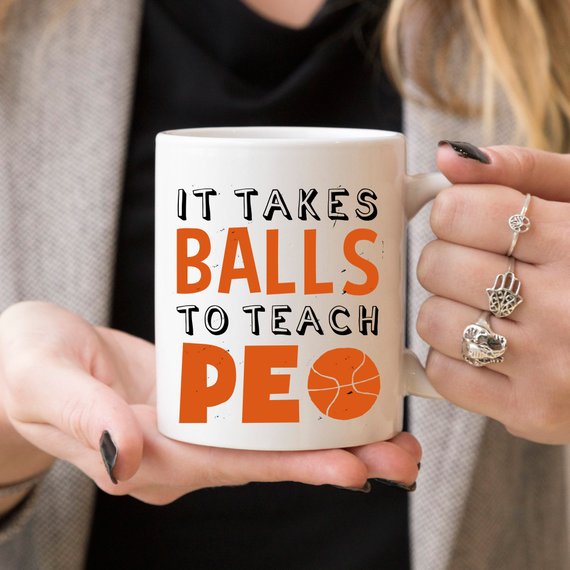 A humorous coffee mug featuring the phrase 'It Takes Balls To Teach PE', crafted from high-quality ceramic, perfect for teachers and sports enthusiasts.