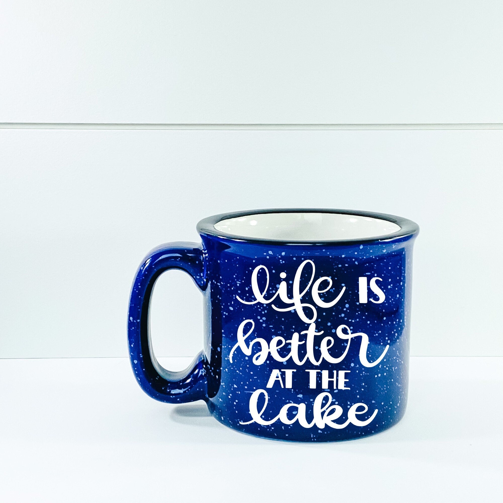 Ceramic campfire mug with 'Life Is Better At The Lake' design, perfect for enjoying beverages by the water.