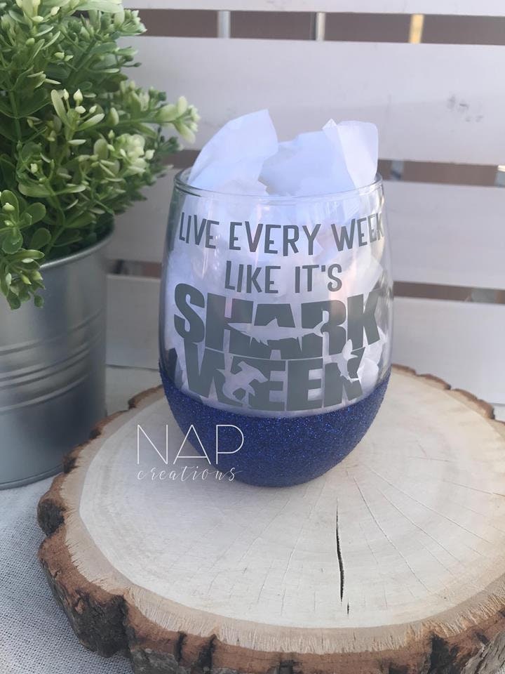 A vibrant stemless wine glass with glitter, featuring the phrase 'Live Every Week Like It's Shark Week' printed on one side.