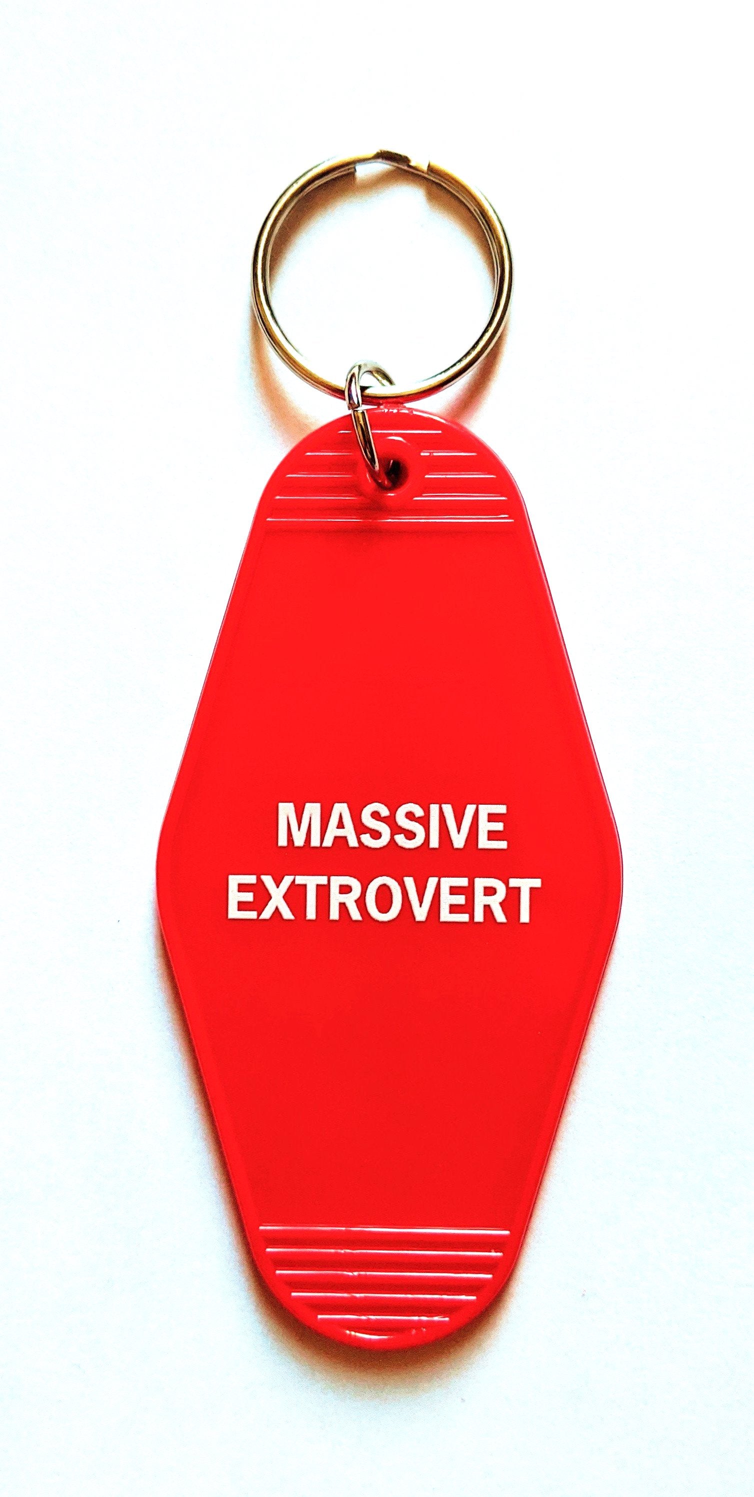 A vibrant red keychain with the words 'Massive Extrovert' in bold white lettering, featuring a classic motel key tag design.