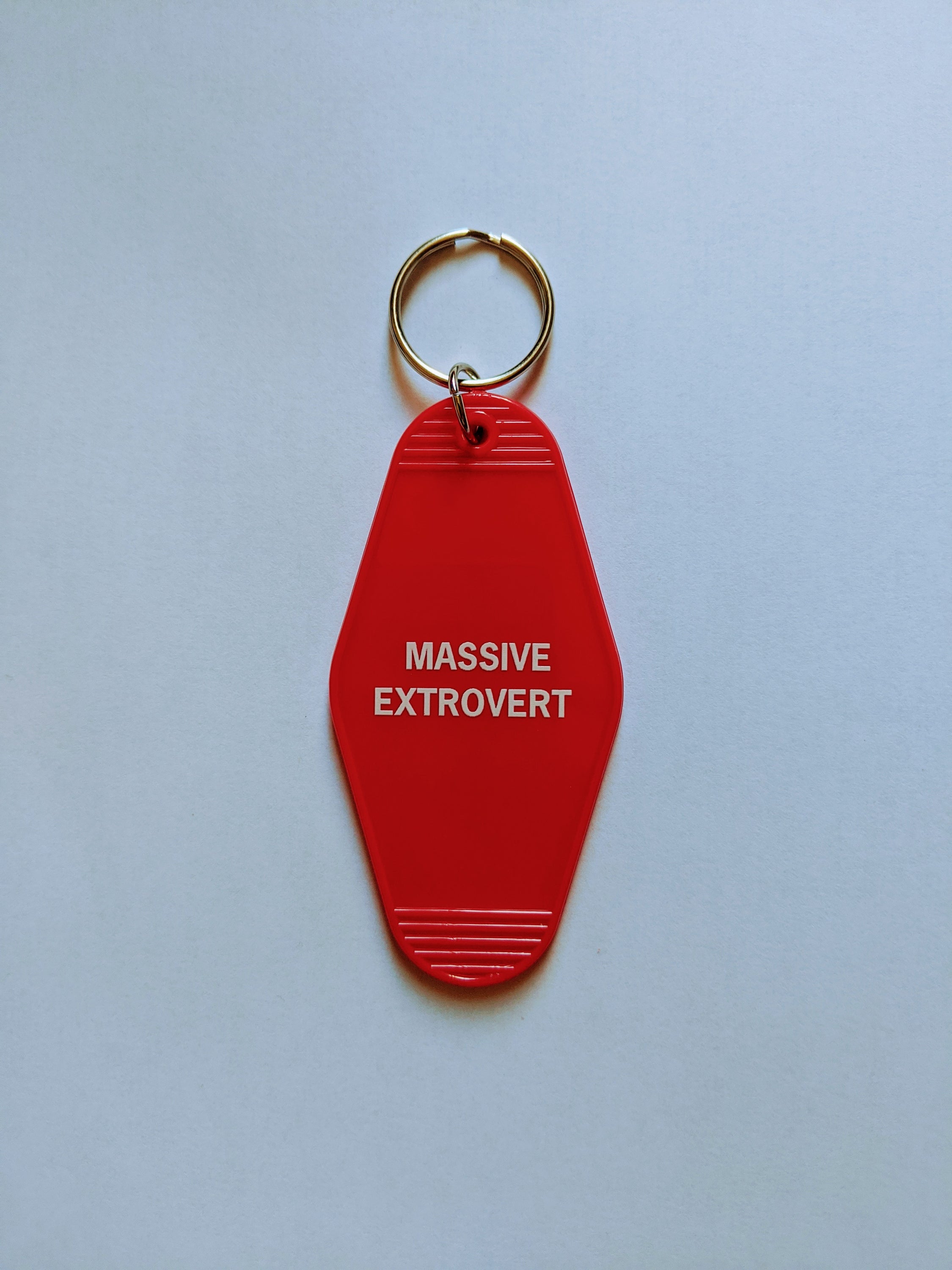 A vibrant red keychain with the words 'Massive Extrovert' in bold white lettering, featuring a classic motel key tag design.