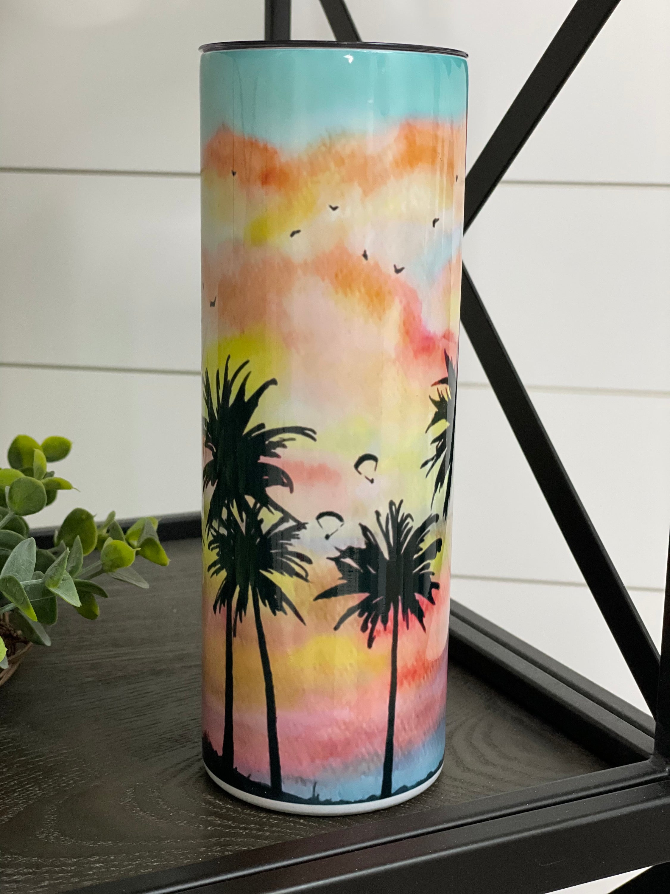 A stylish 20oz skinny tumbler featuring a vibrant palm tree painting design, perfect for hot and cold beverages.