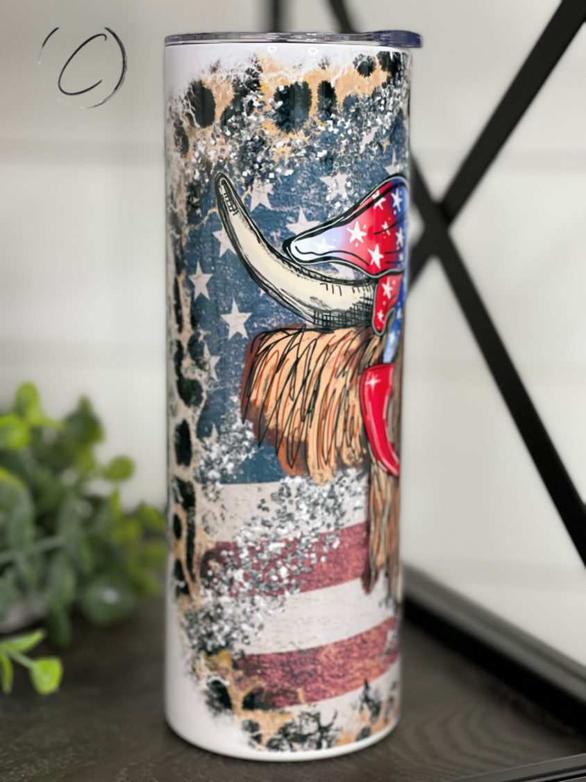 A 20oz skinny tumbler featuring a vibrant patriotic Highland cow design, perfect for hot and cold beverages.