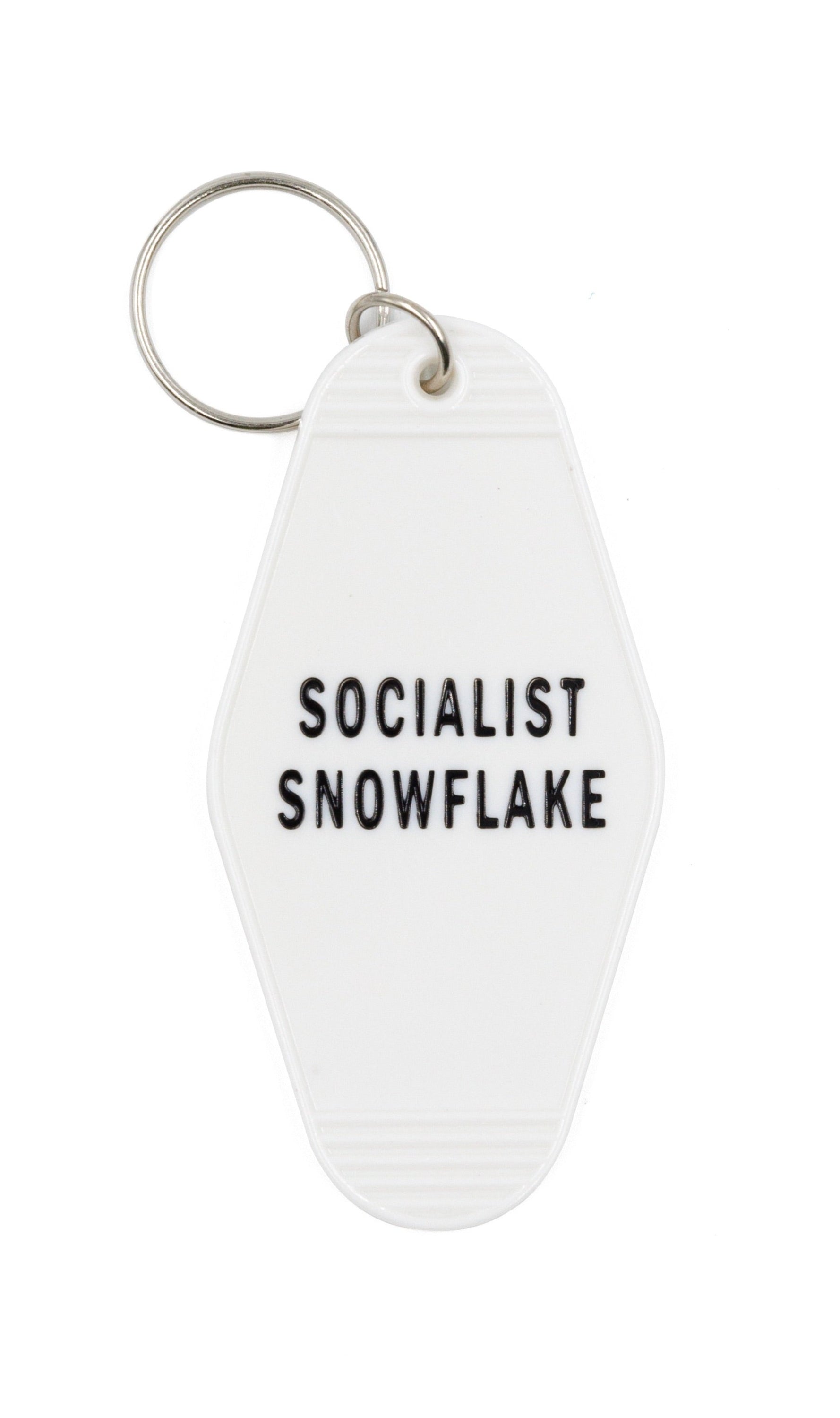 A white motel-style keychain with 'SOCIALIST SNOWFLAKE' in black lettering, featuring a split ring for key attachment.