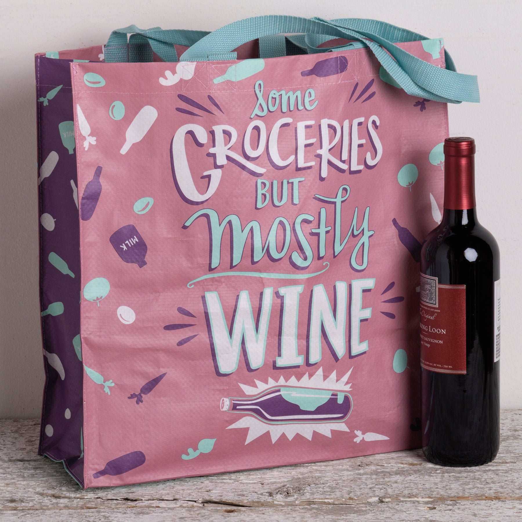 A large market tote bag in pink and blue featuring the phrase 'Some Groceries But Mostly Wine' with veggie and wine bottle designs.